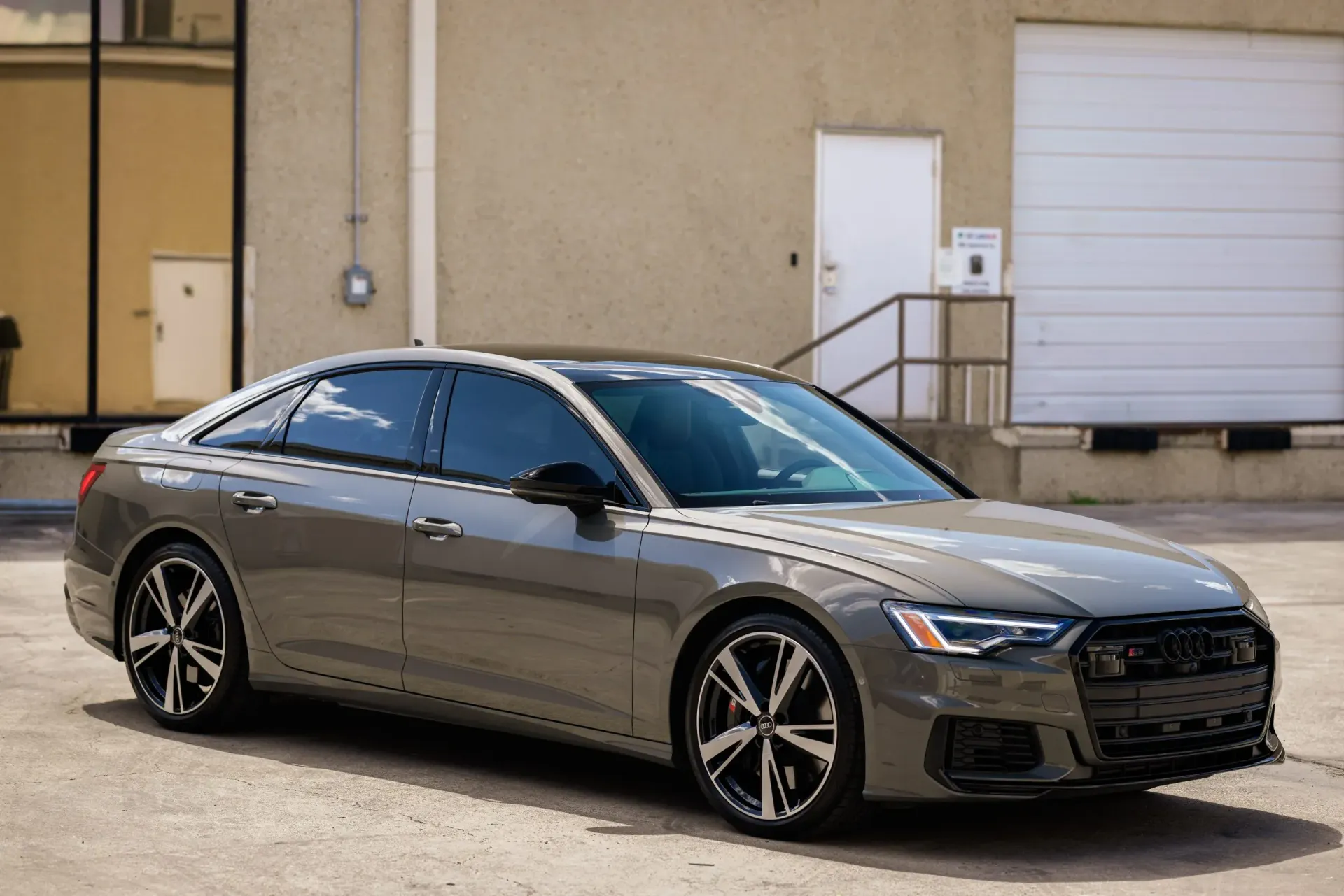 Gray Audi sedan parked in front of a tan building with a white door and loading dock.