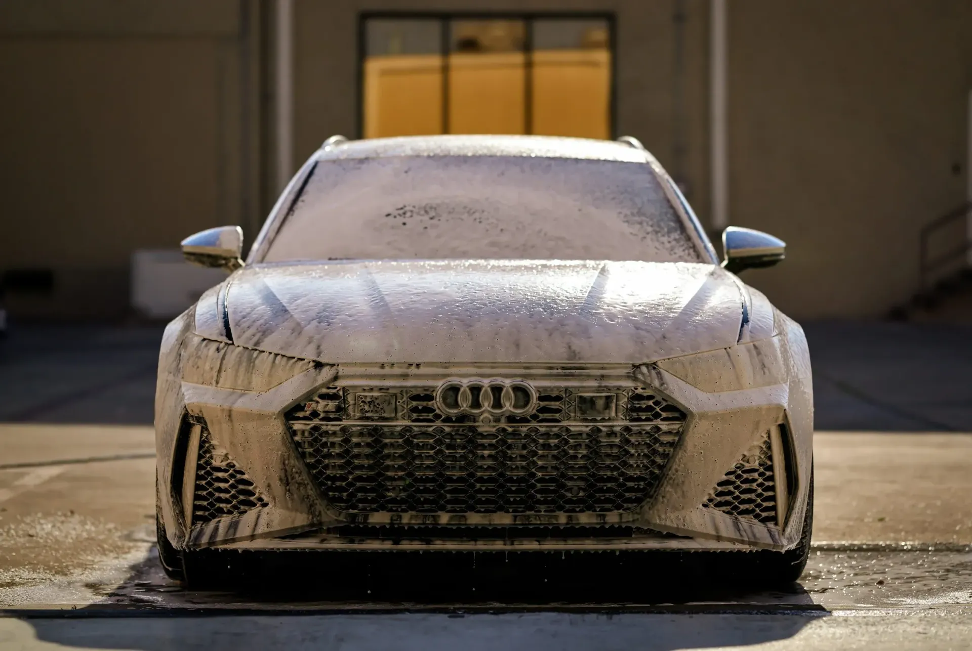 Audi RS6 covered in white foam, front view, outdoors.