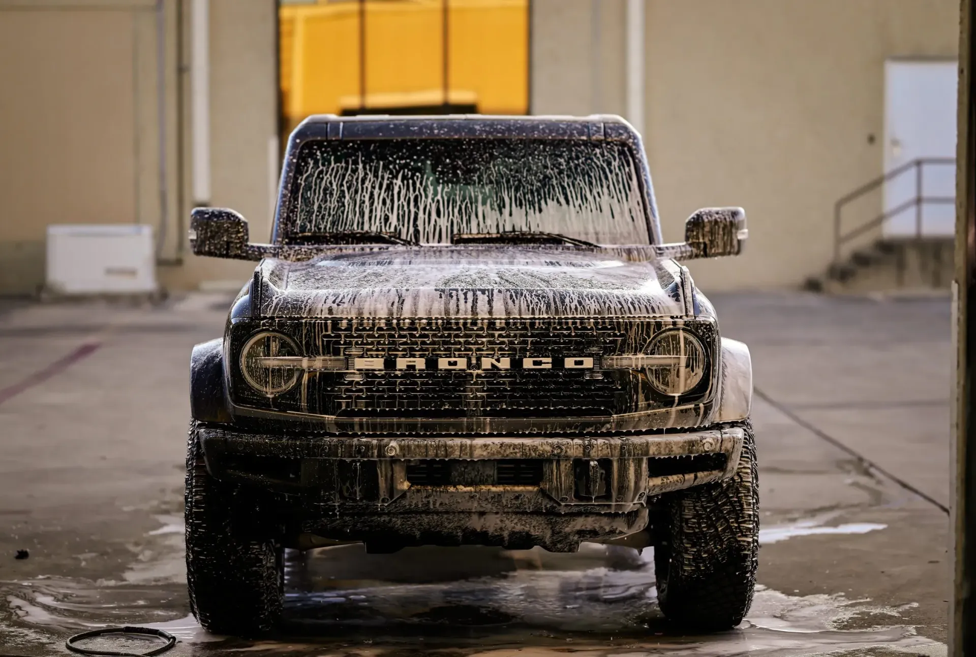 Ford Bronco covered in soap suds at a car wash.