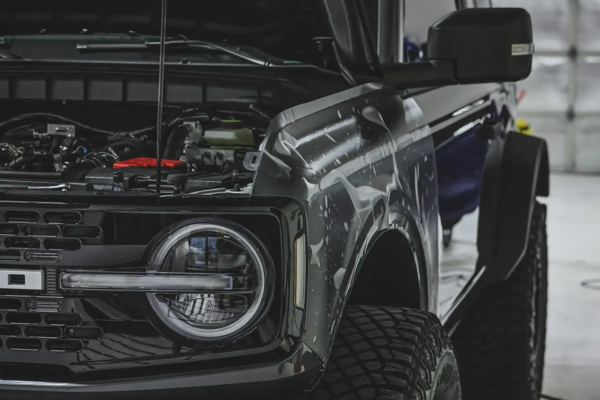 Black Ford Bronco with open hood, in a garage.