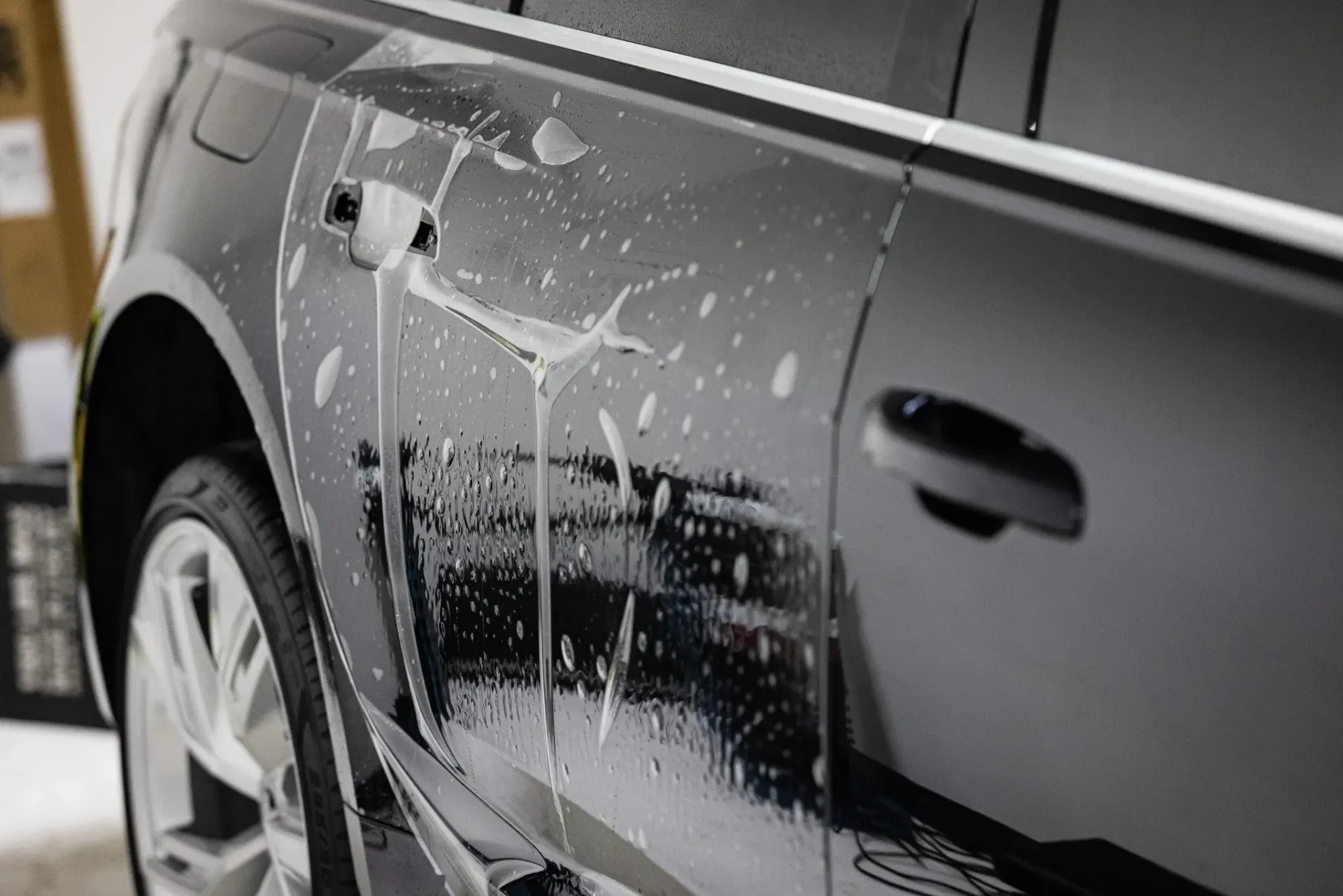 Black car door being treated with a clear protective film, water dripping down.
