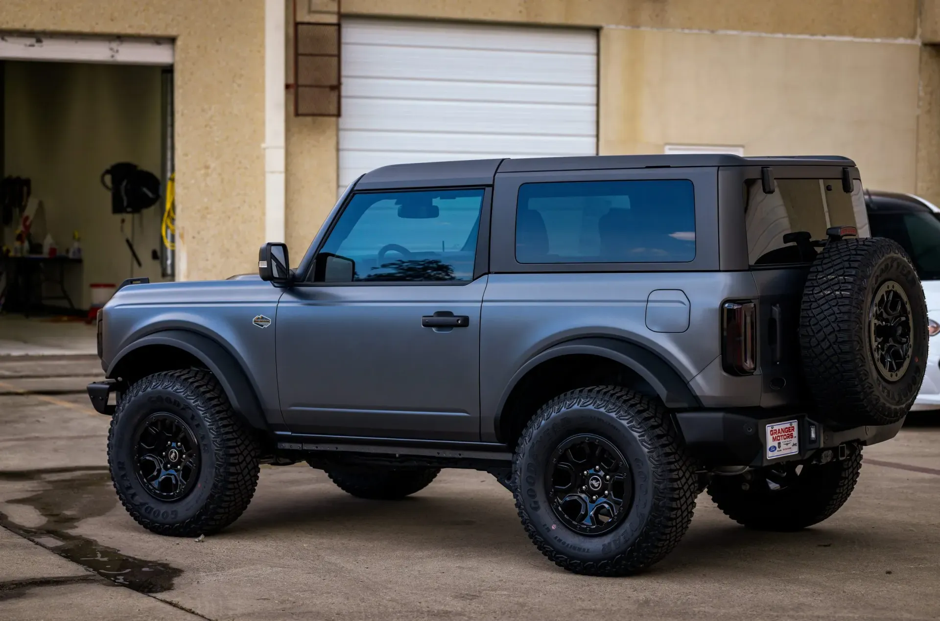 Gray Ford Bronco with black wheels and a spare tire parked outdoors.