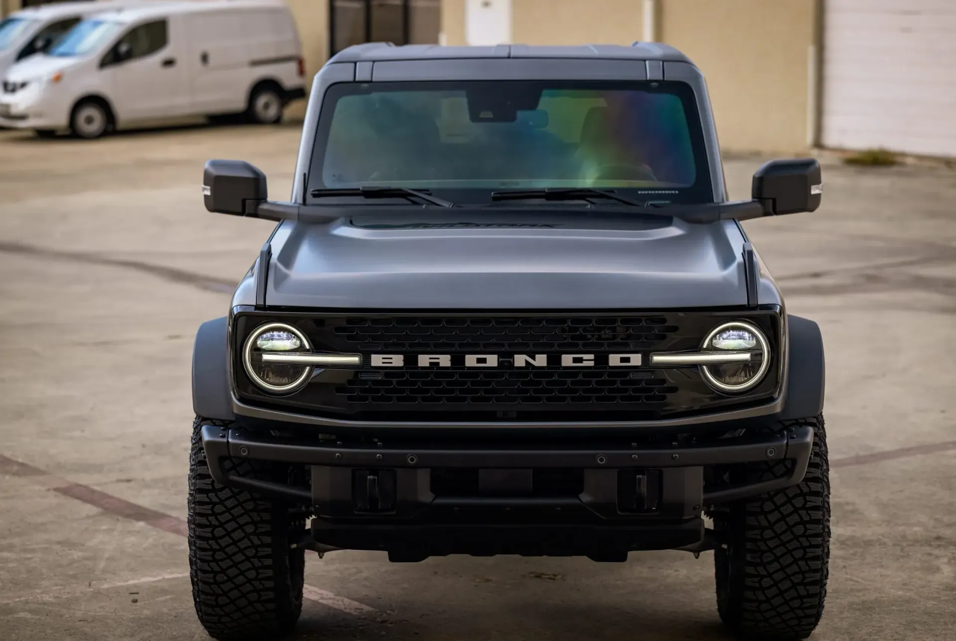 Black Ford Bronco, front view, outdoors. Round headlights, Bronco name on grill, dark tires.