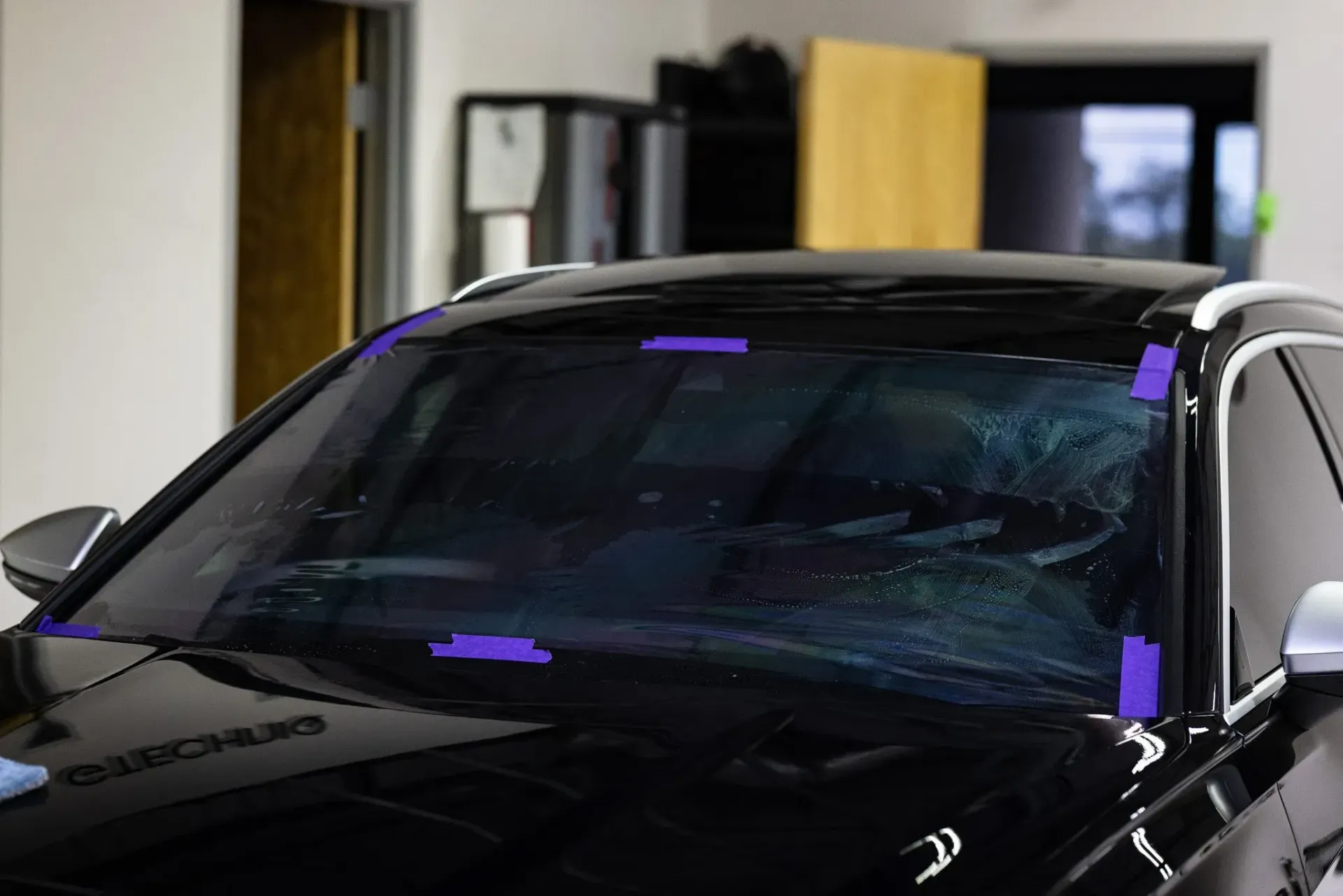 Black car windshield with purple tape, being tinted inside a shop.