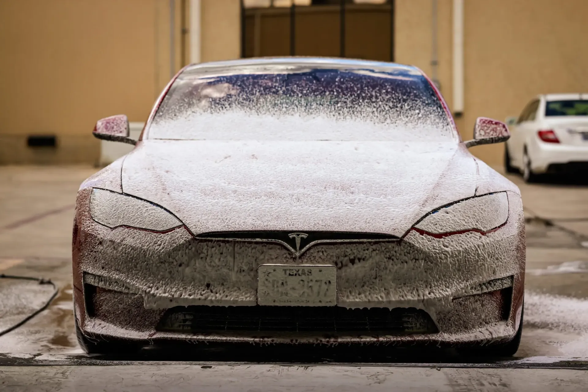 Tesla car covered in white foam during a wash.