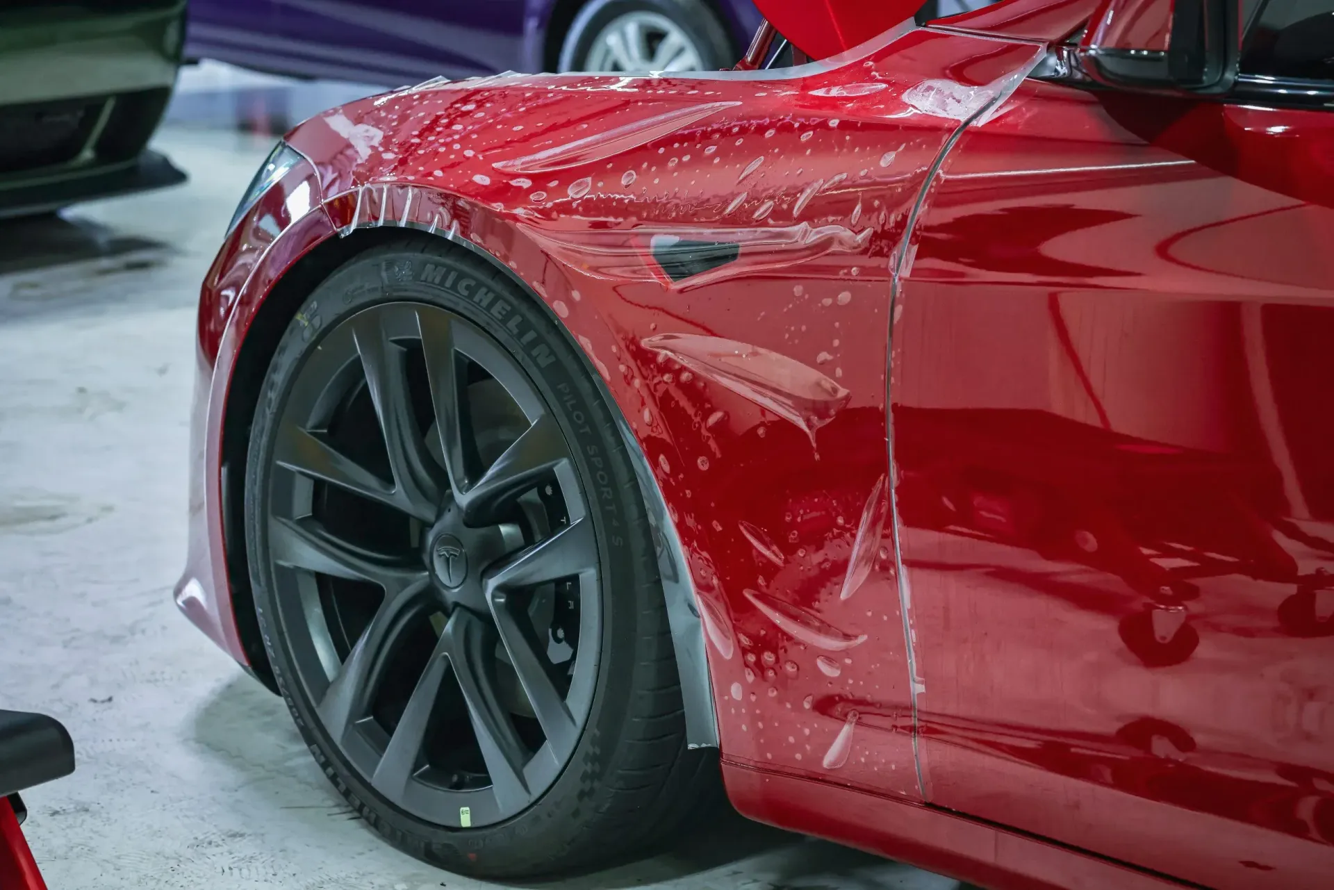 Red Tesla car with protective film being applied to the front panel.