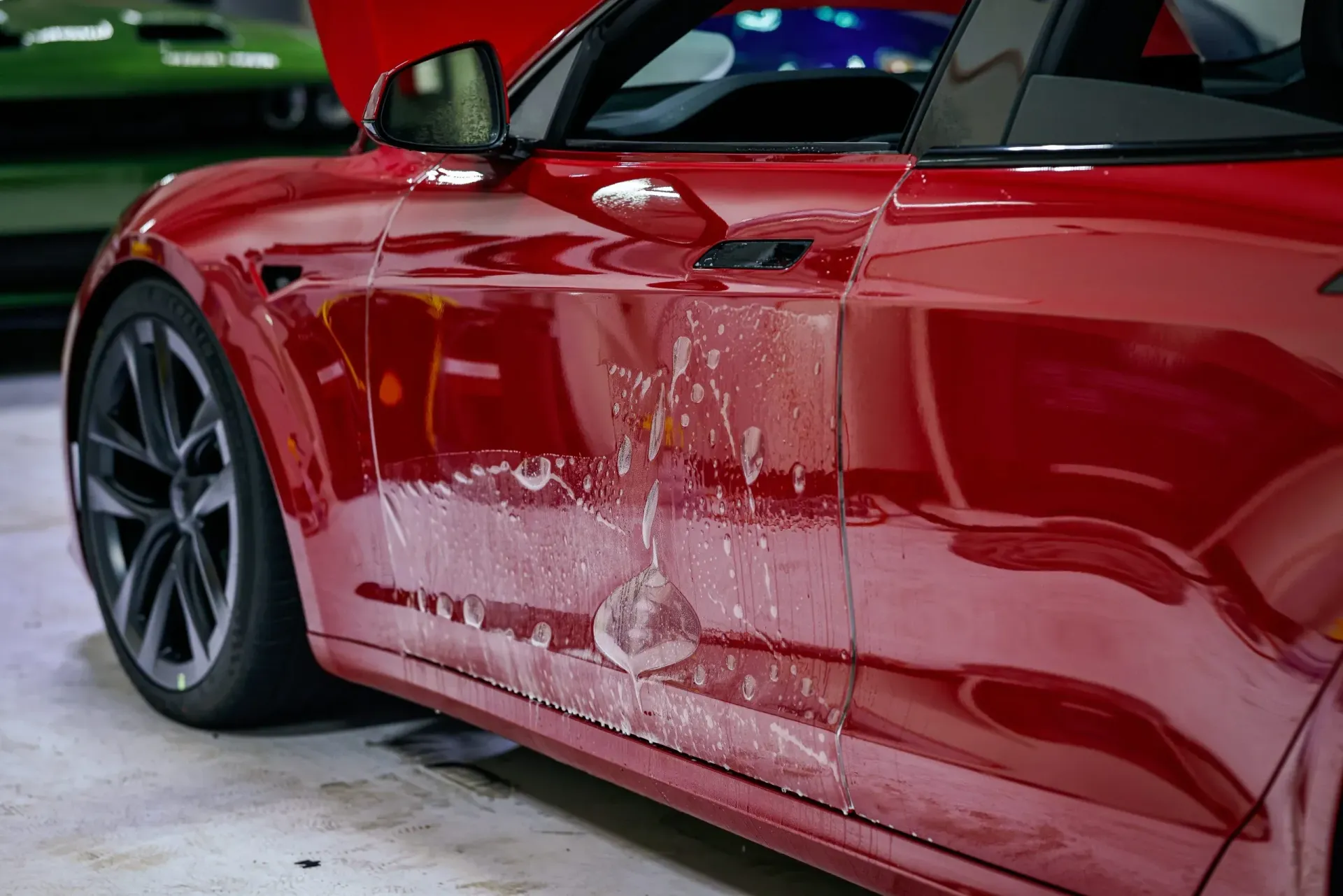 Red Tesla car with water droplets on the side in a garage.