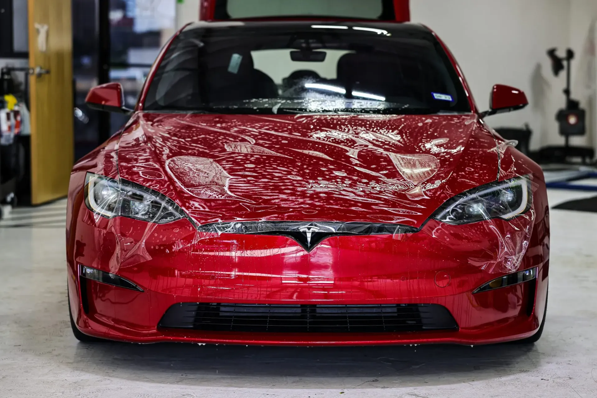 Red Tesla being covered with a clear protective film in a garage.