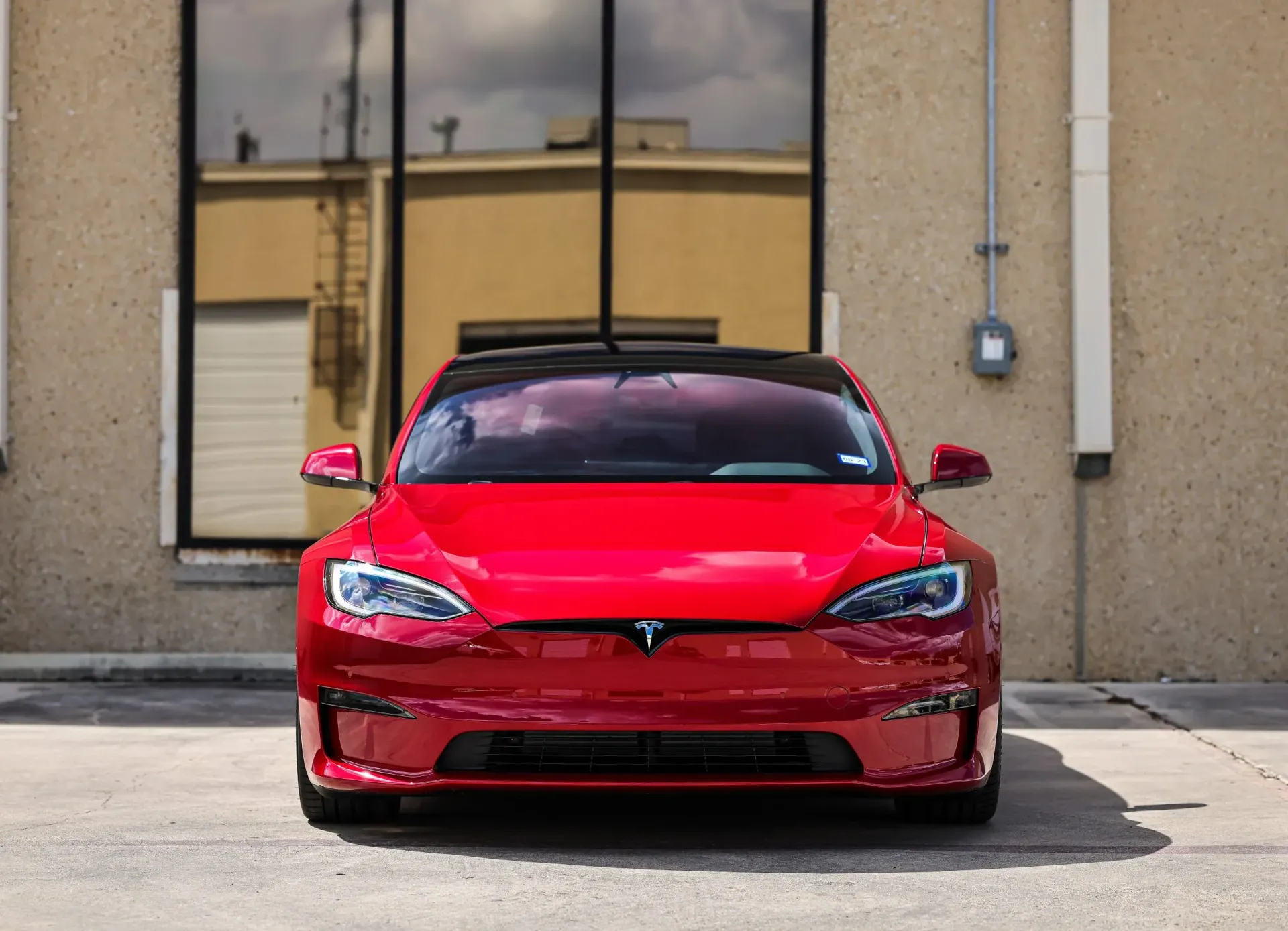 Red Tesla parked in front of a beige building with a glass window.
