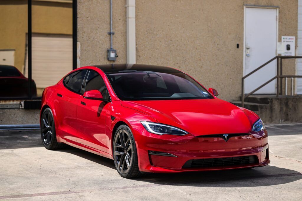 Red Tesla Model S parked in front of a building with black wheels and a black roof.
