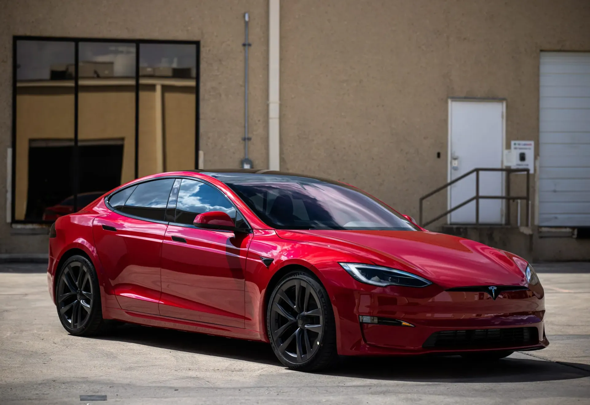 Red Tesla Model S parked in front of a building with black wheels and tinted windows.
