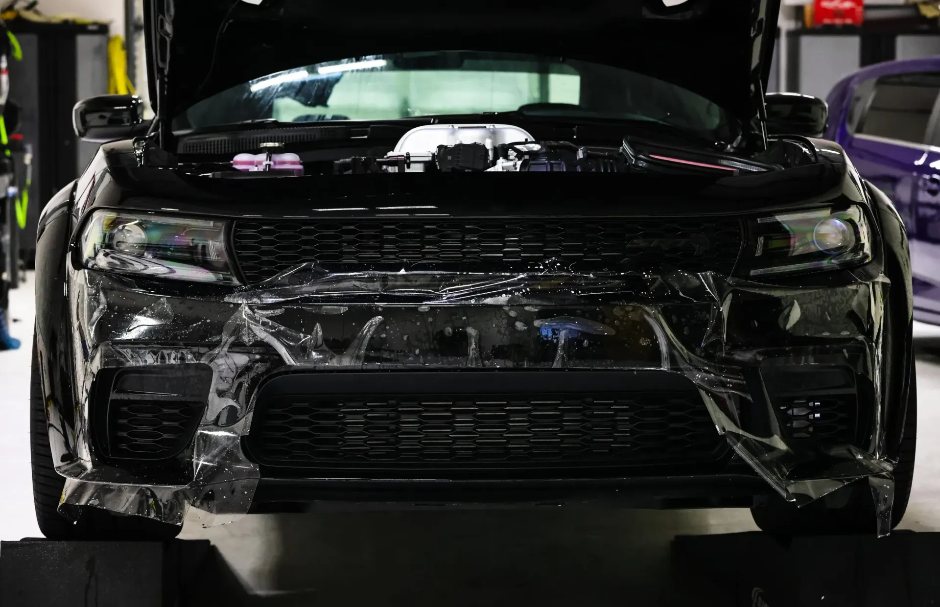 Black car with hood up, front bumper covered in clear protective film.