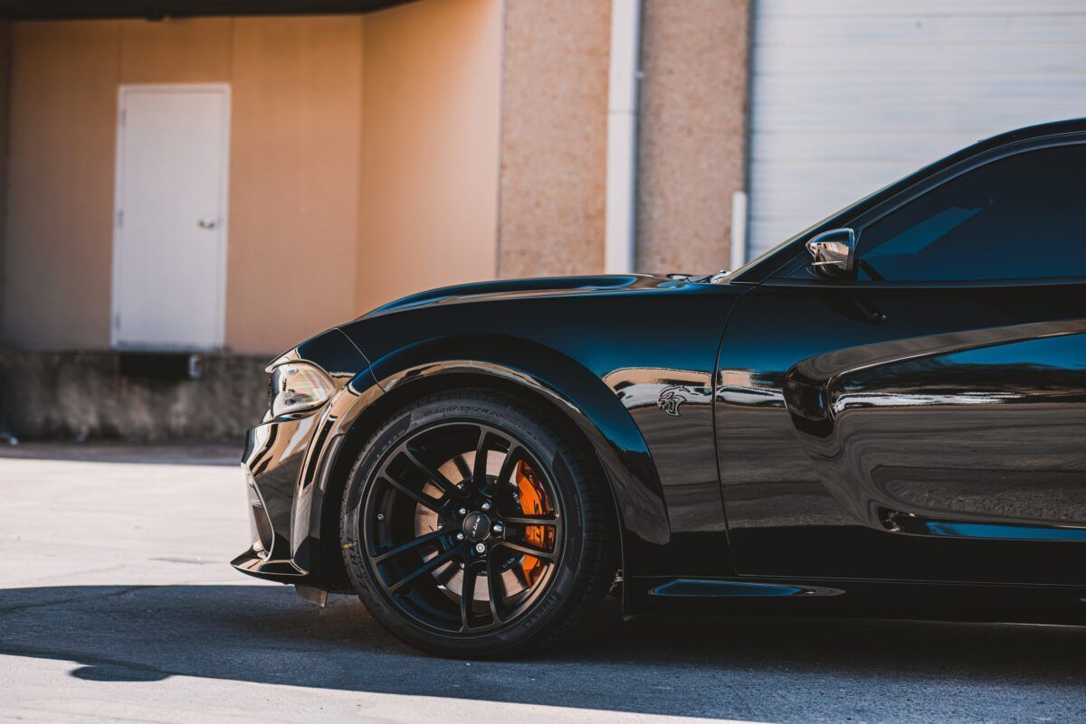 Black Dodge Charger with orange brake calipers parked in front of a building.