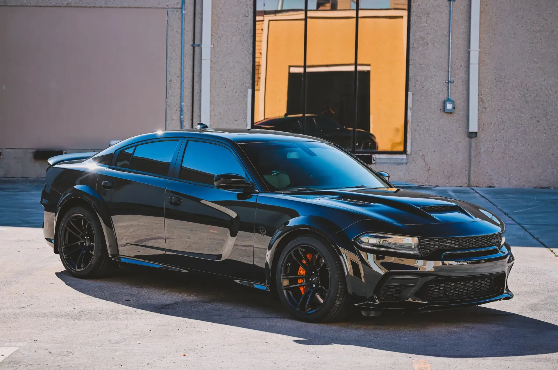 Black Dodge Charger parked in front of a building with orange brake calipers visible.