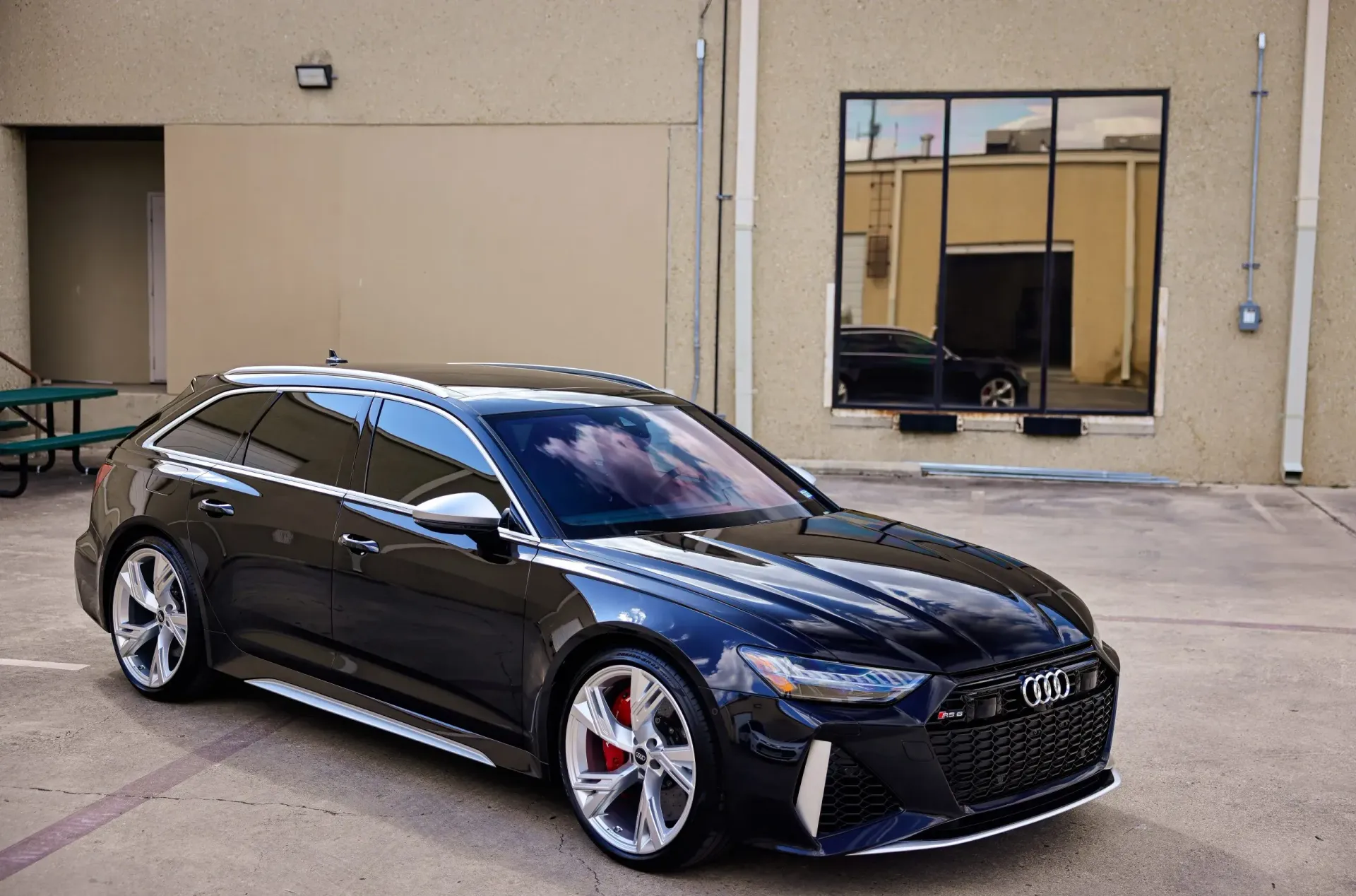 Black Audi RS6 Avant parked outside a building, reflecting in the windows.