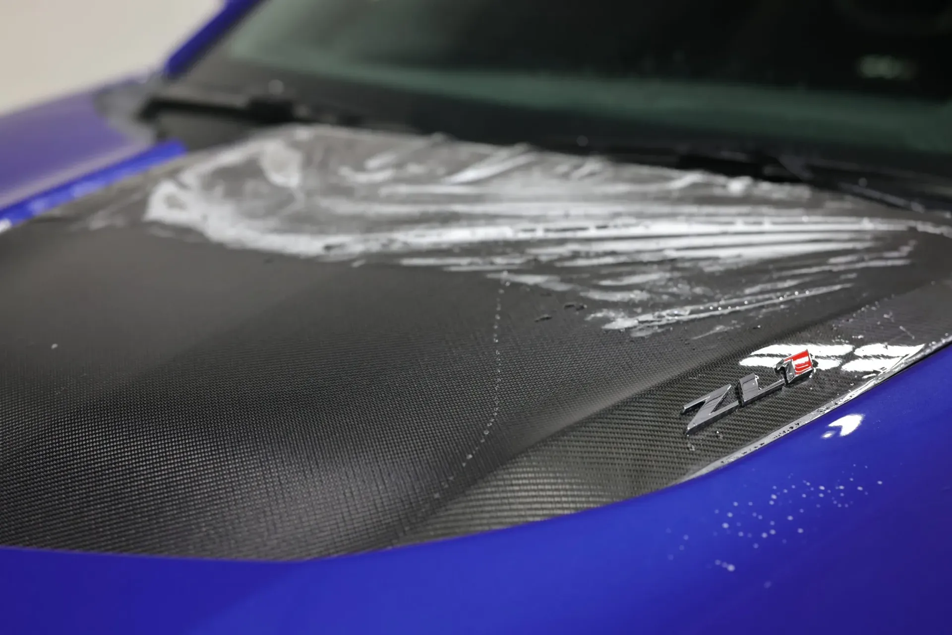 Blue car hood with carbon fiber scoop, covered with soapy water, ZL1 logo visible.