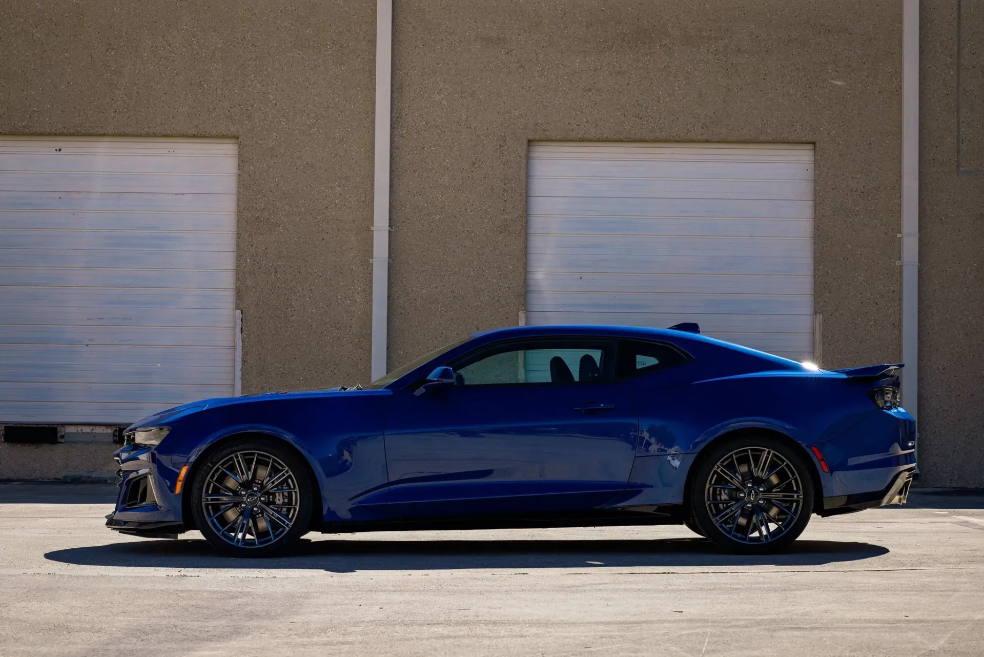 Blue sports car parked outside a building with closed garage doors.