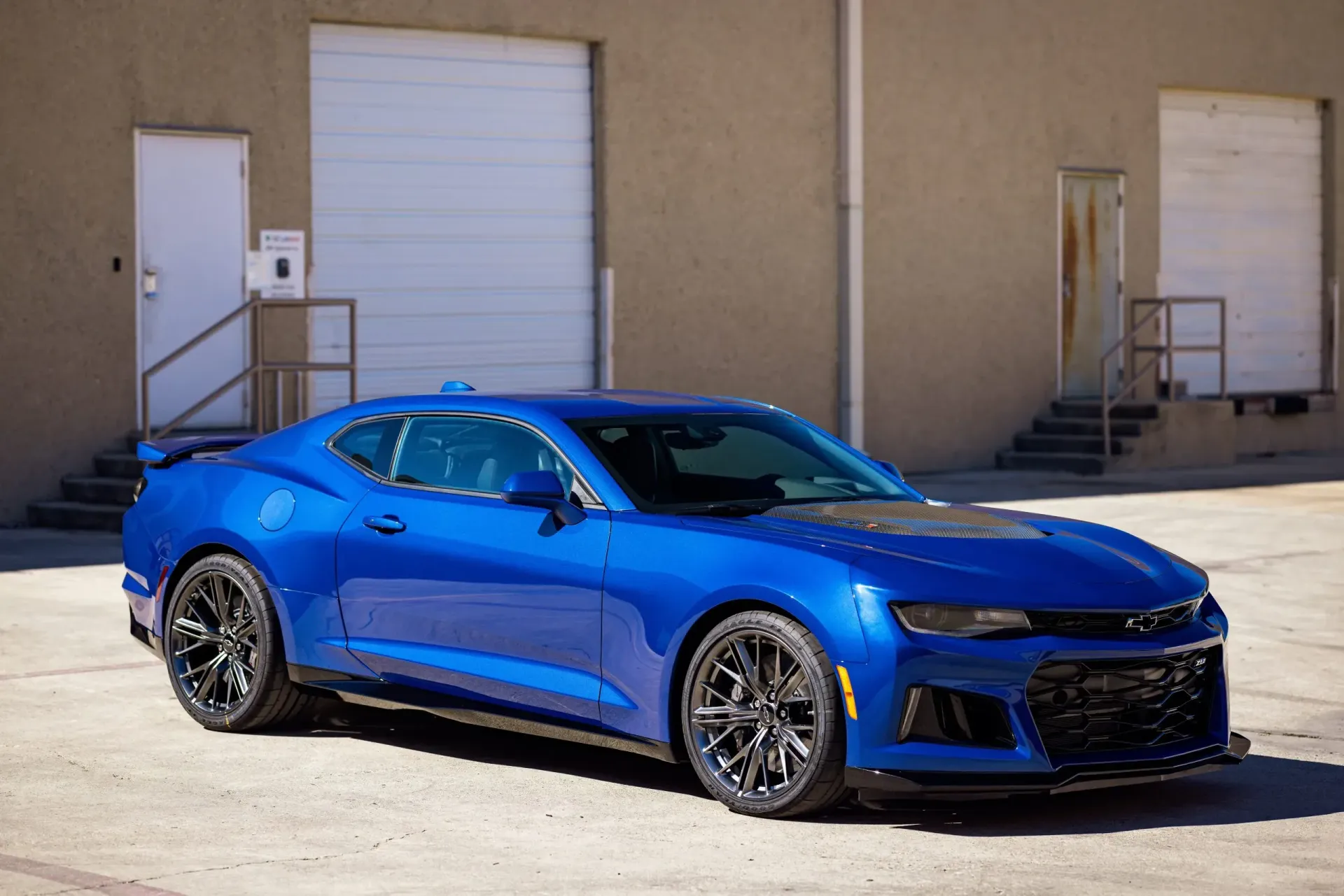 Blue Chevrolet Camaro parked in front of a building with a closed garage door.