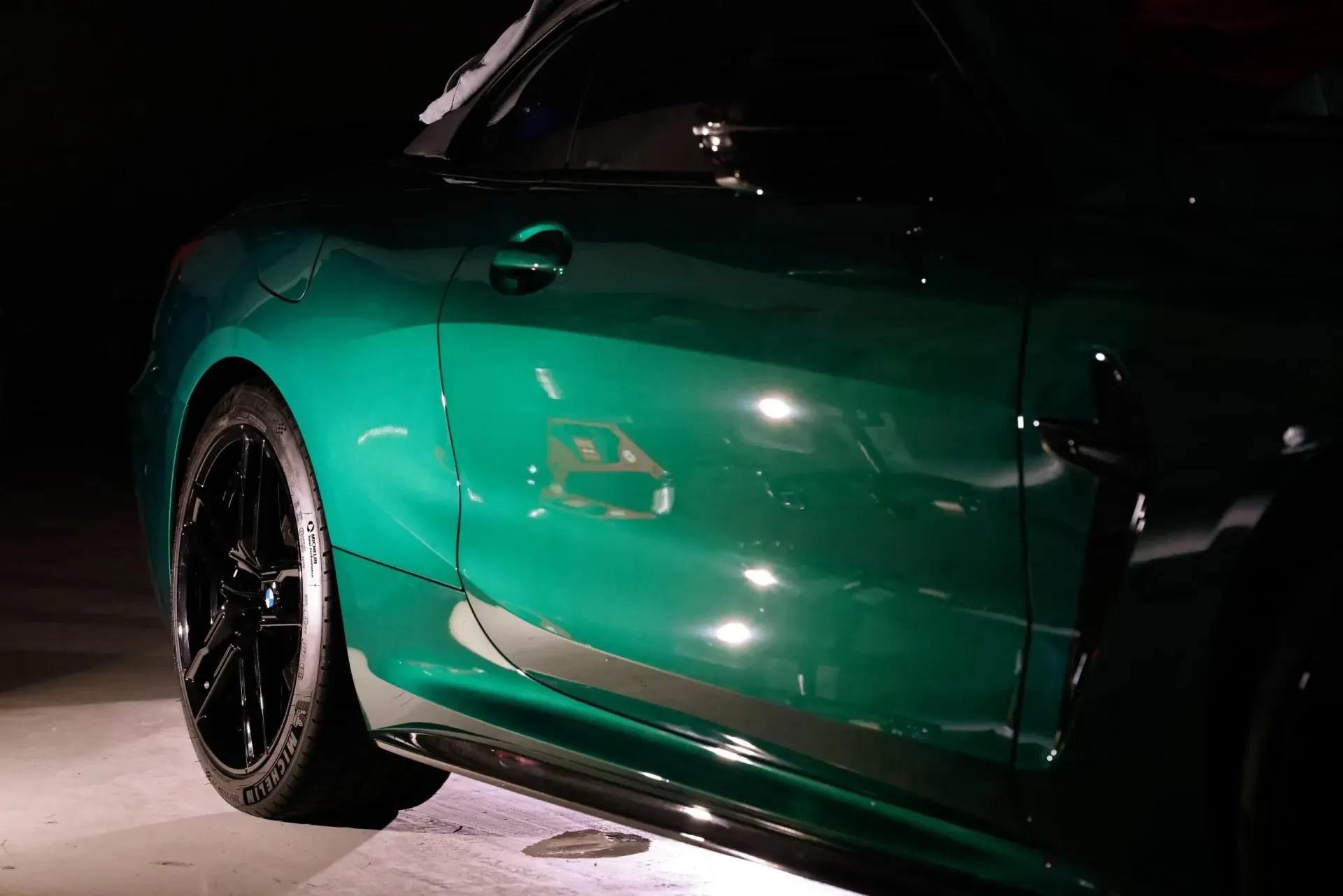 Green sports car, side view, with shiny paint and black wheels, lit dimly.