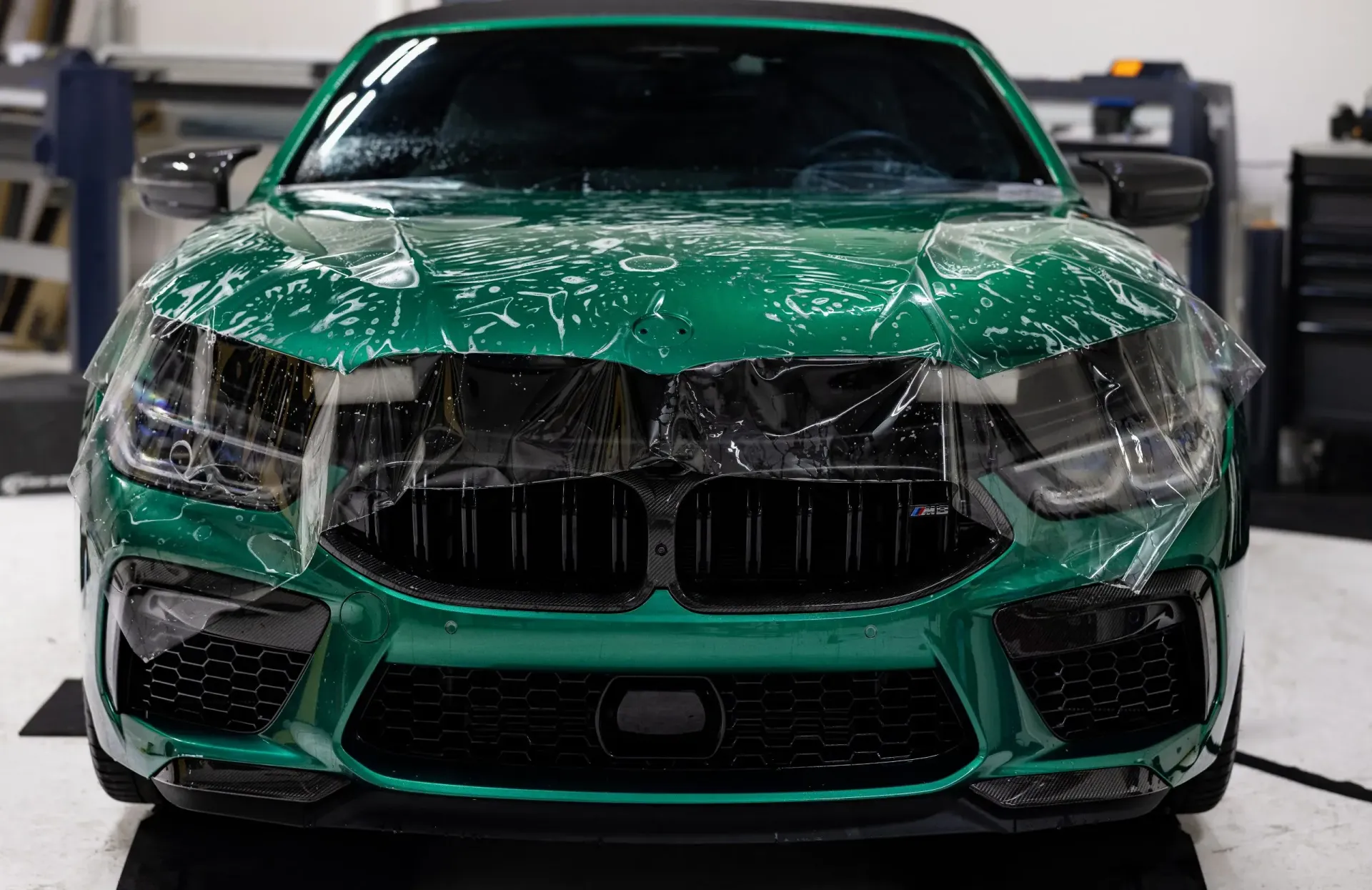 Green BMW car front with protective film in a garage.