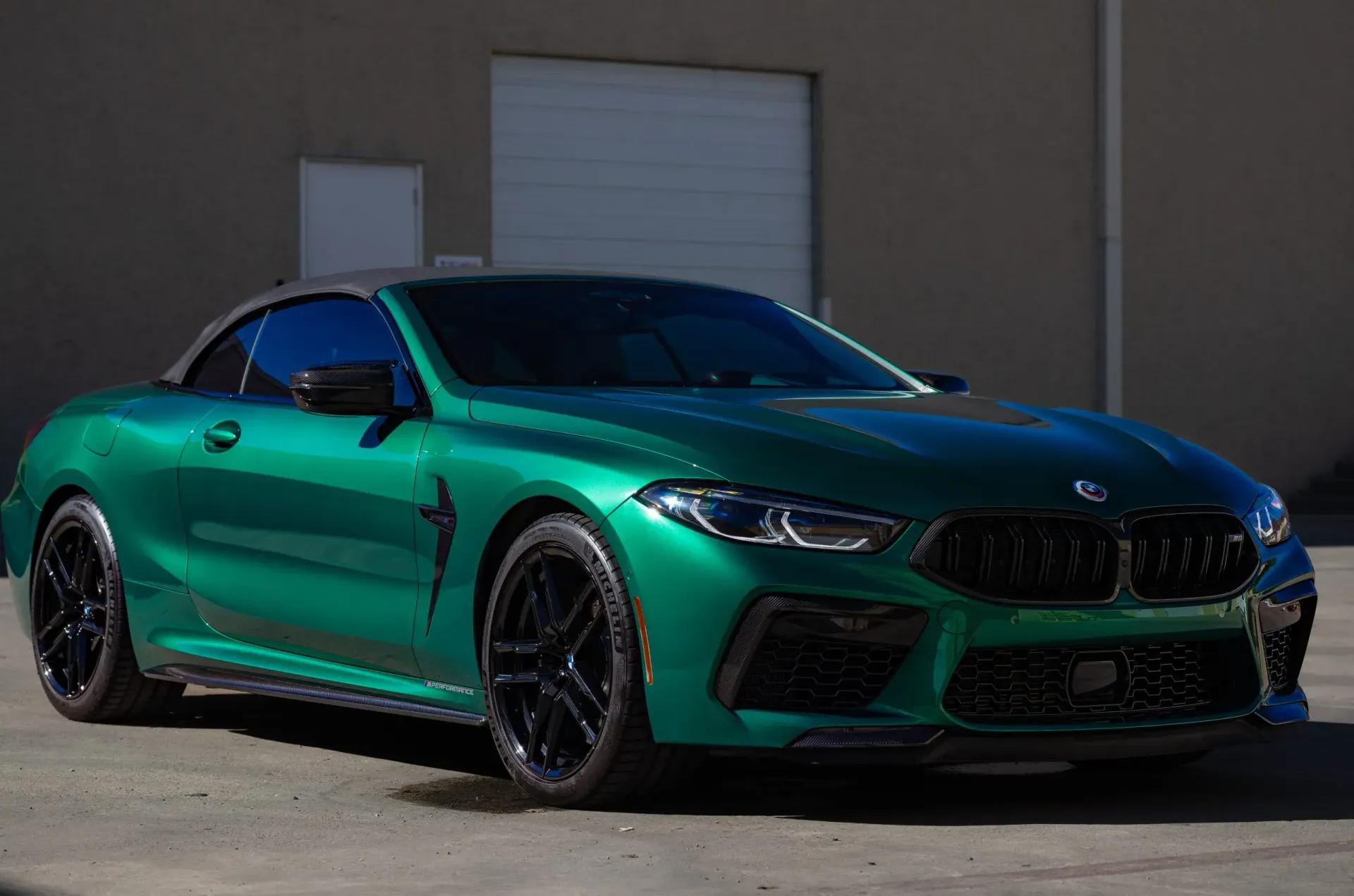 Emerald green BMW M8 convertible, black wheels, parked in front of a building.