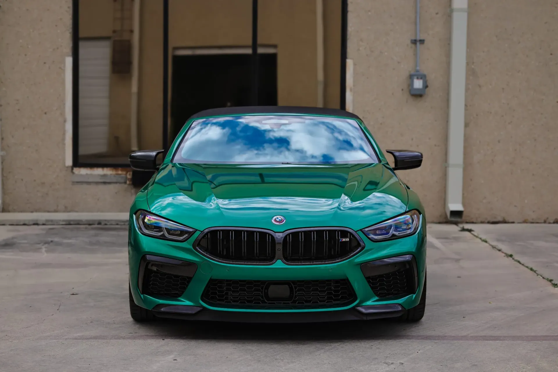 Green BMW M8 parked in front of a building, reflecting the sky in its windshield.