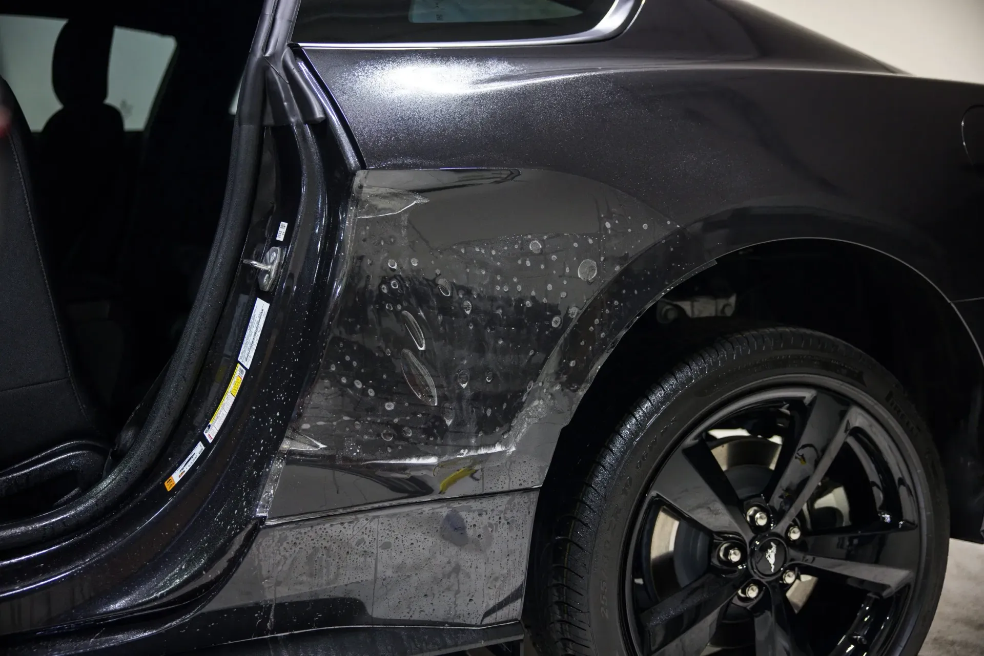 Black car with visible scratches and door open, near a tire.