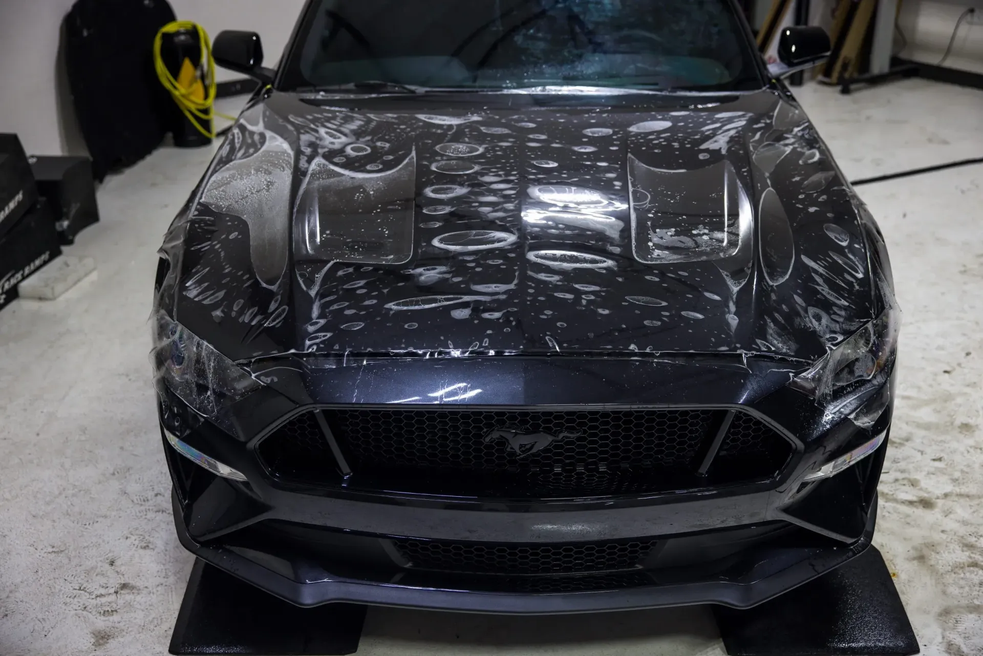 Black car hood with protective film applied, indoors.