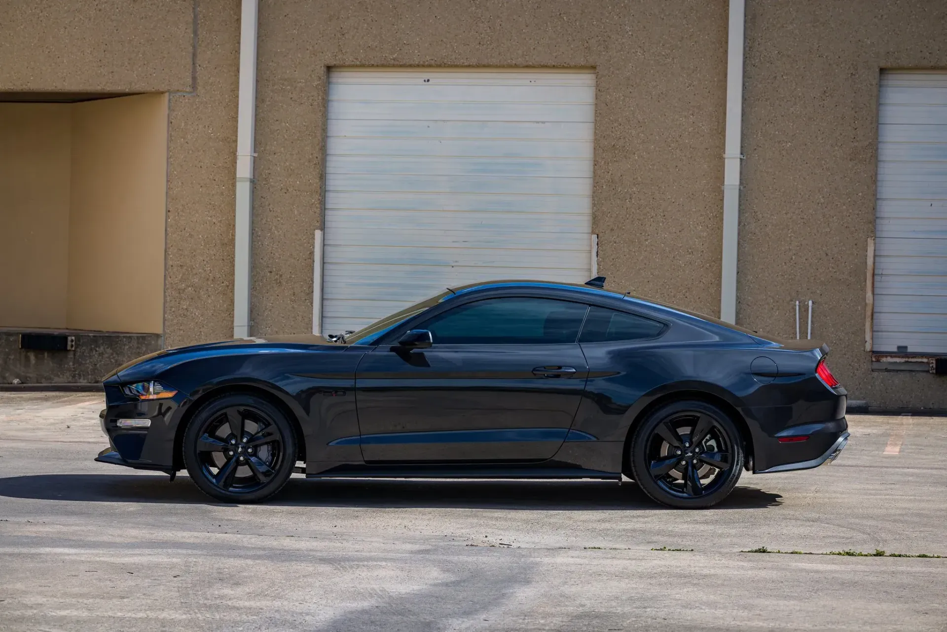 Black Ford Mustang made of blocks, parked in front of a tan industrial building.
