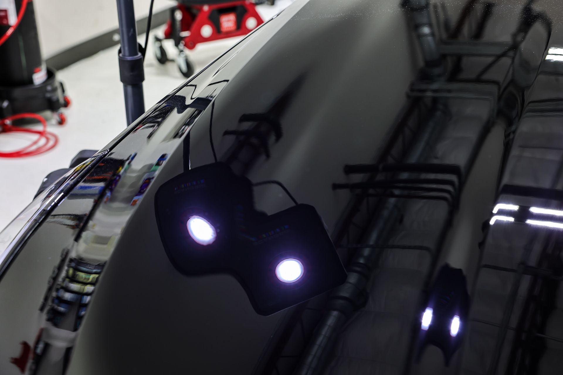Black car hood reflects two bright lights, showing detail work in a garage.