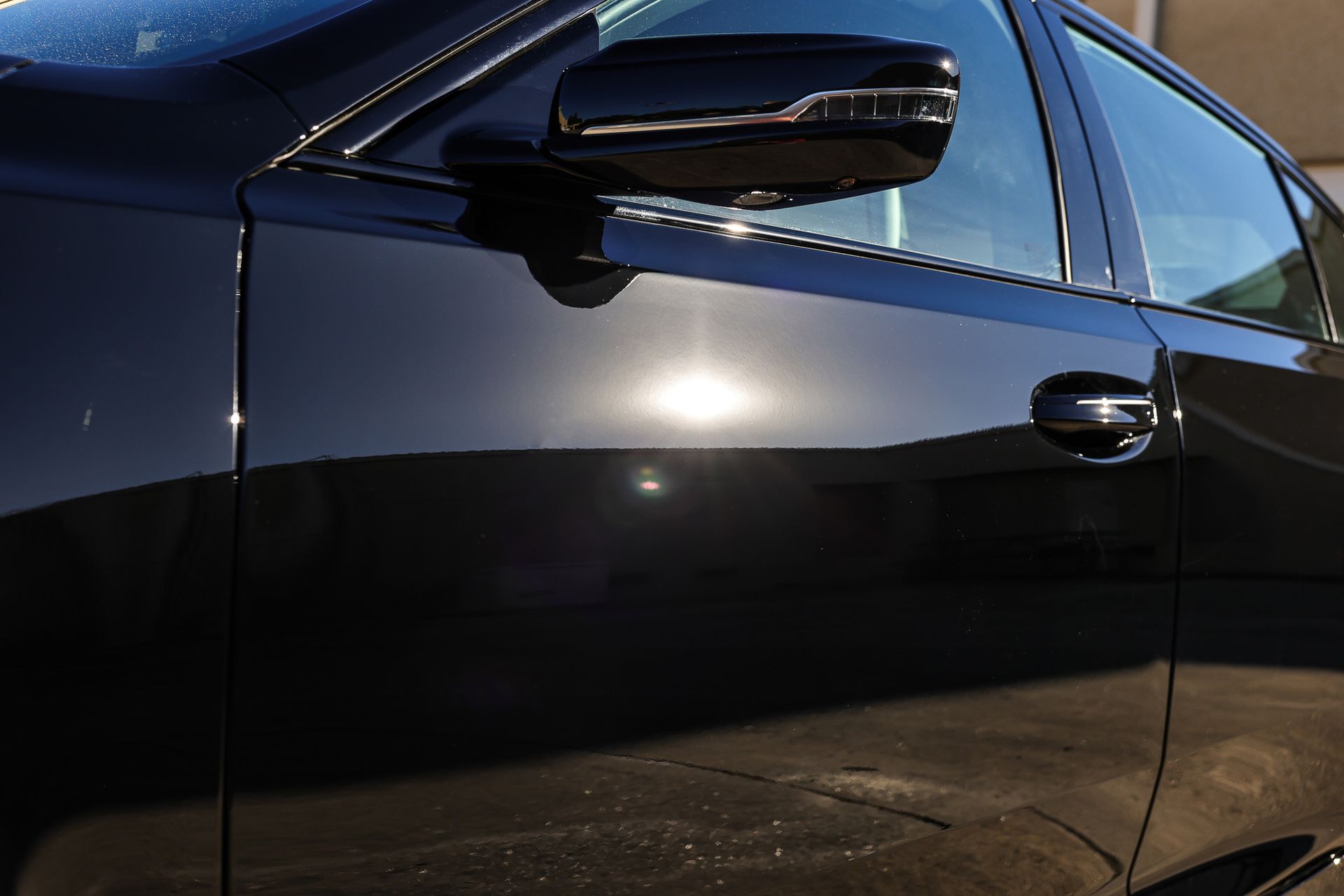 Black car door with shiny paint, side mirror, and sunlight reflection.