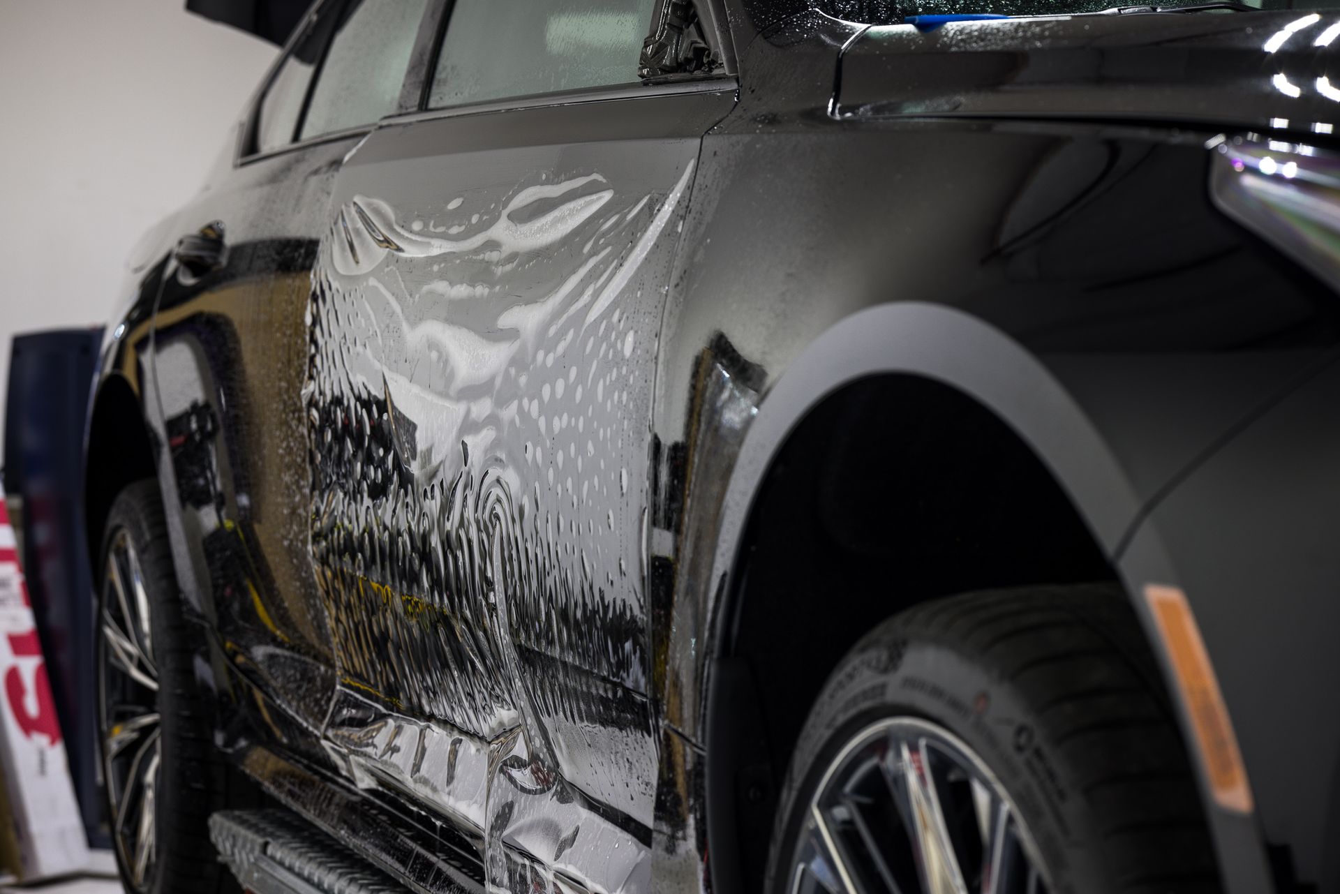 Black car being covered with a clear protective film in a garage.