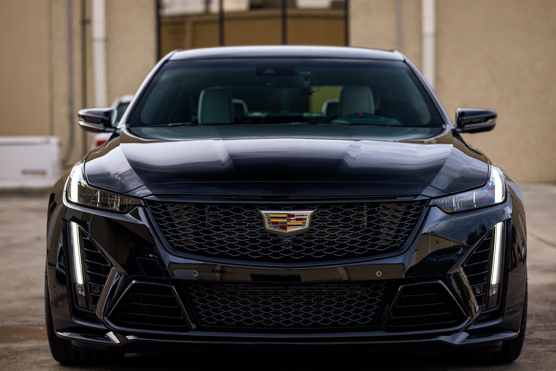 Black Cadillac sedan, front view, parked in front of building, headlights on.