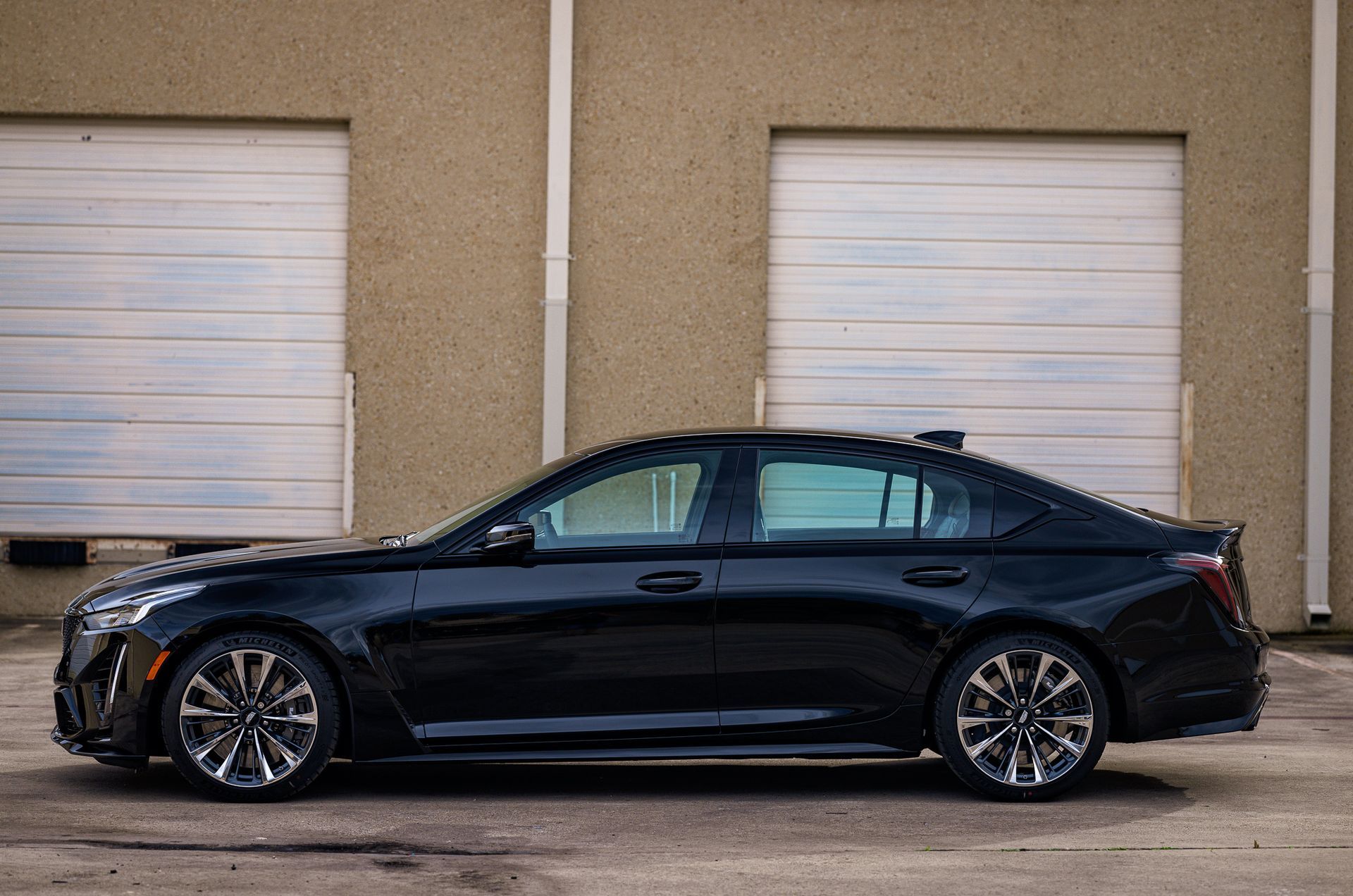 Black Cadillac sedan parked in front of a beige building with closed garage doors.