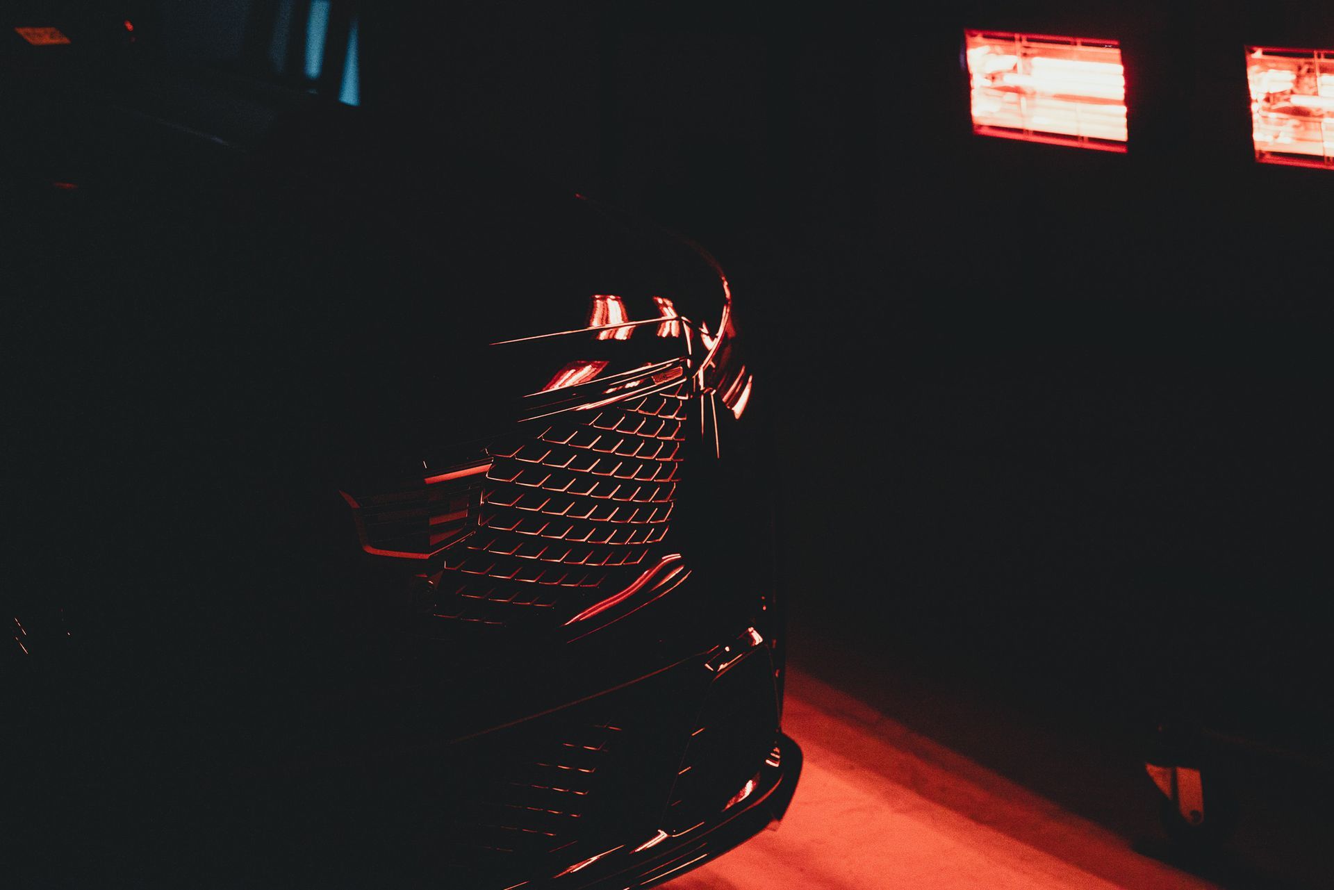 Dark car front, red grill, red-lit garage.