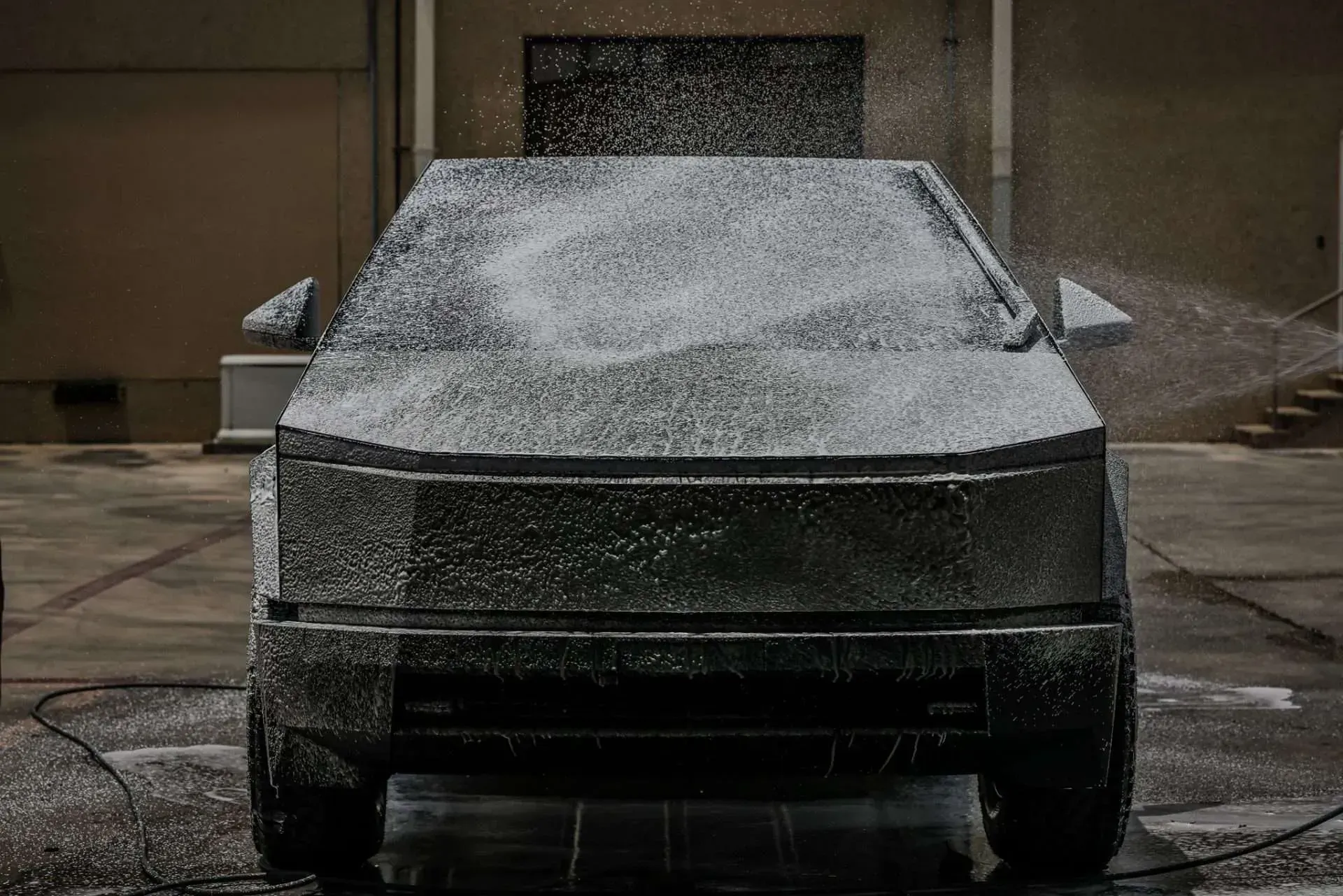 Tesla Cybertruck covered in soapy foam, being washed outdoors.