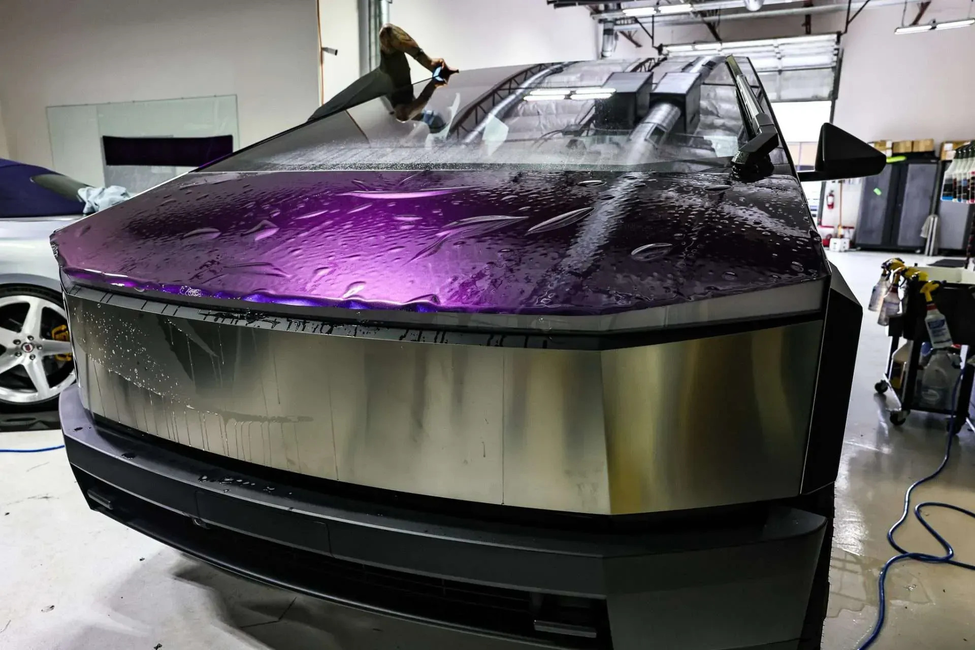Tesla Cybertruck being wrapped with purple and silver film in a shop.