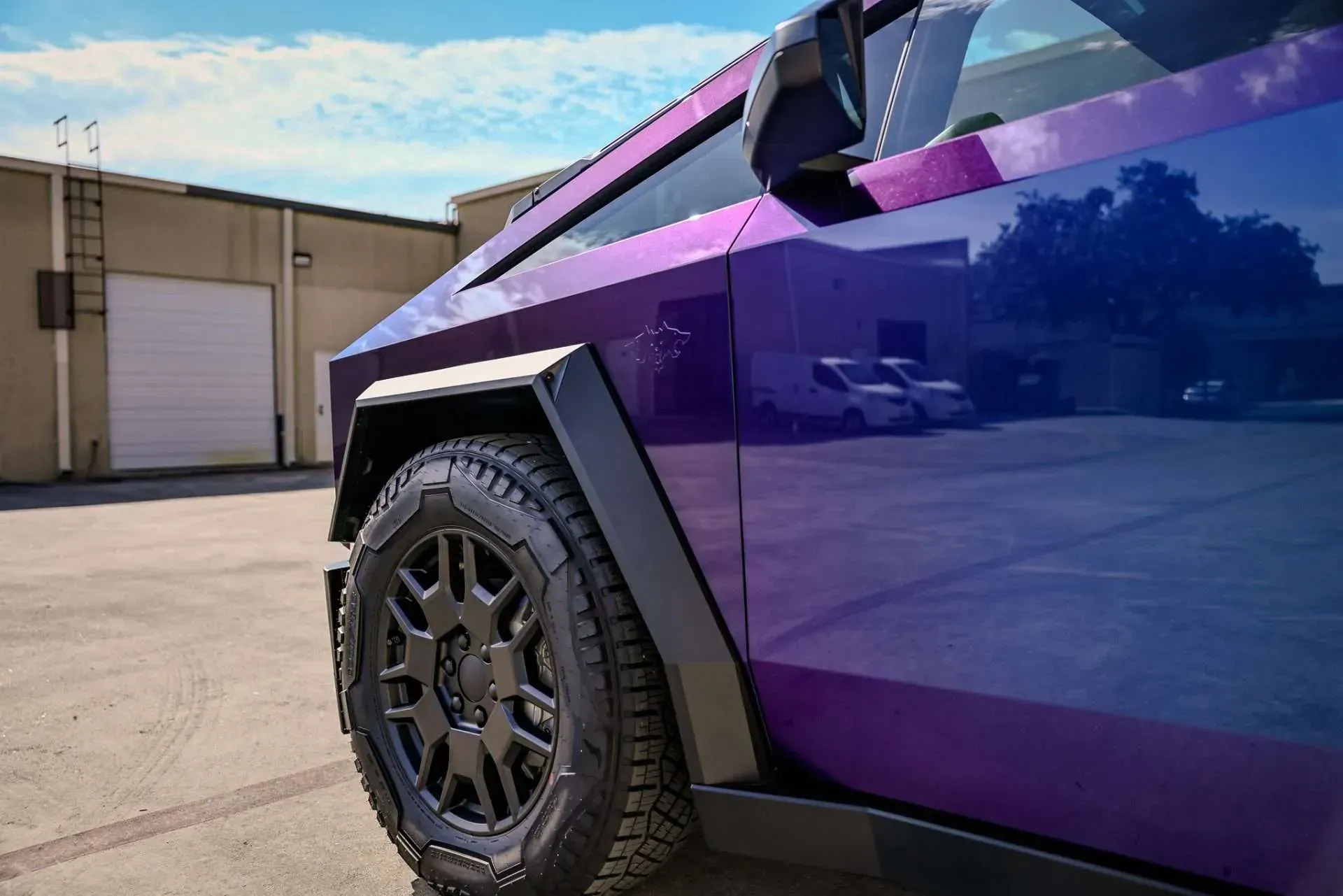 Purple Tesla Cybertruck with black accents and off-road tires, parked in front of a building.