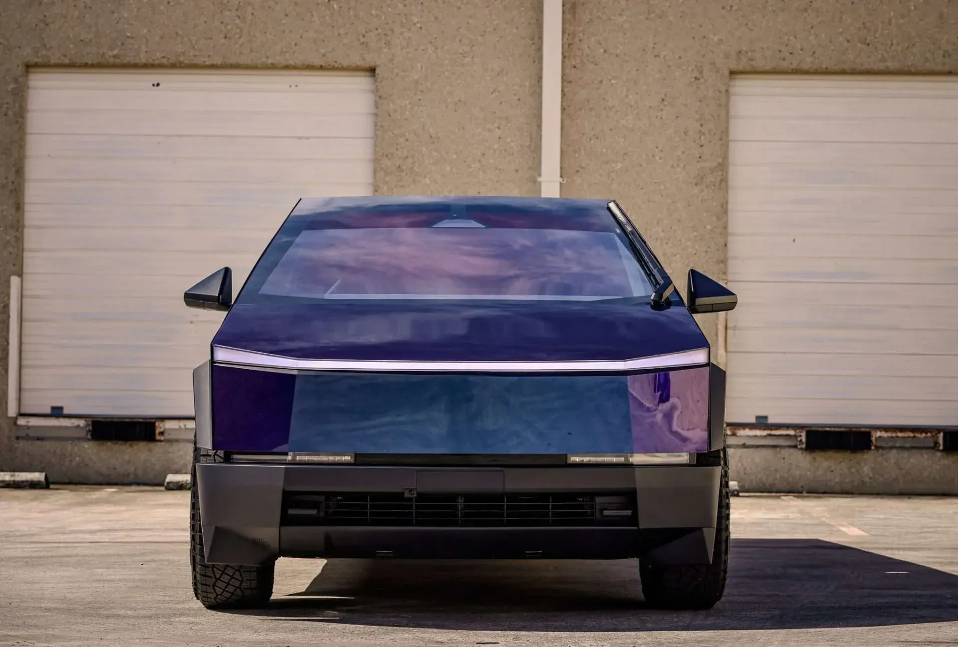 Blue Tesla Cybertruck parked in front of a building with closed garage doors.