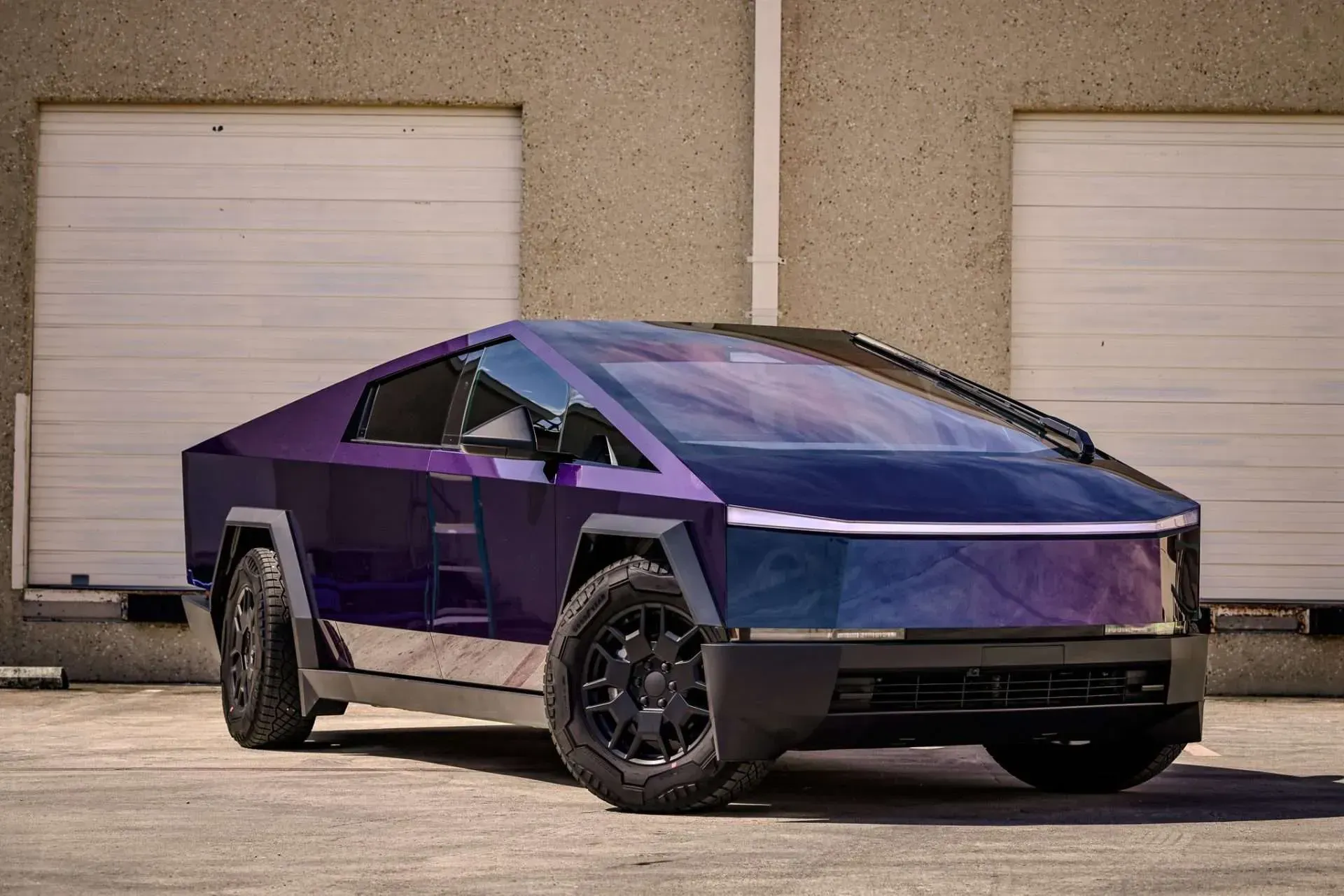 Purple-wrapped Tesla Cybertruck parked outside, angled front view.