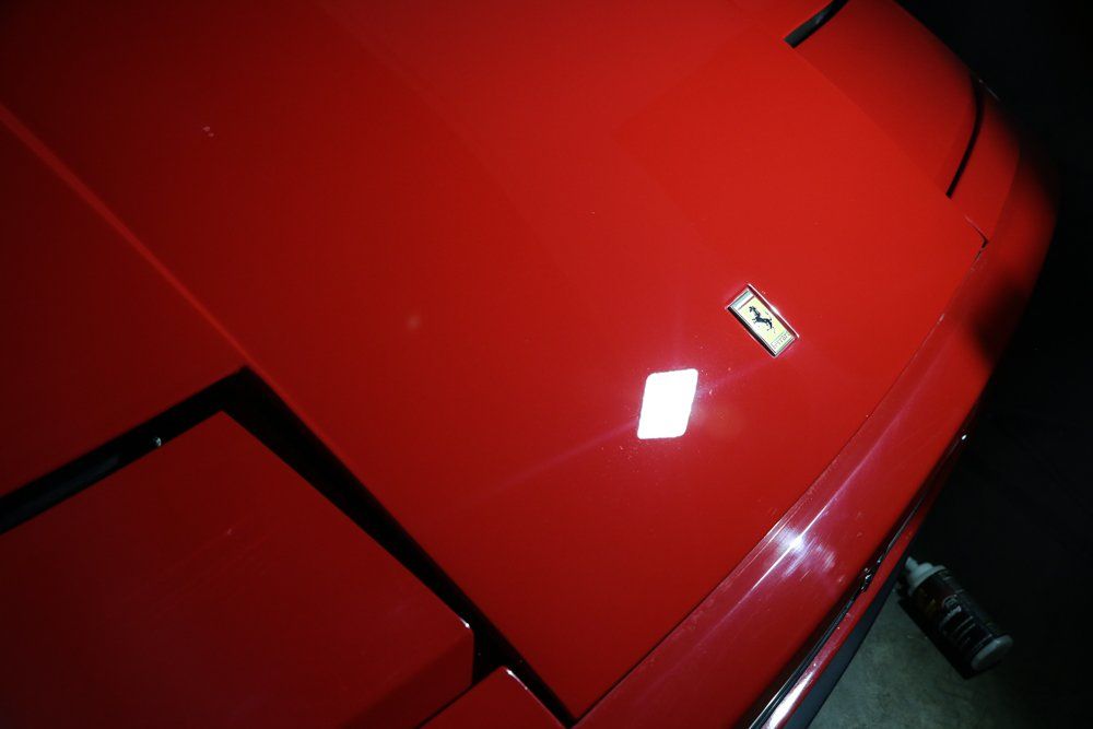 Red Ferrari car hood with the Ferrari emblem reflecting light.