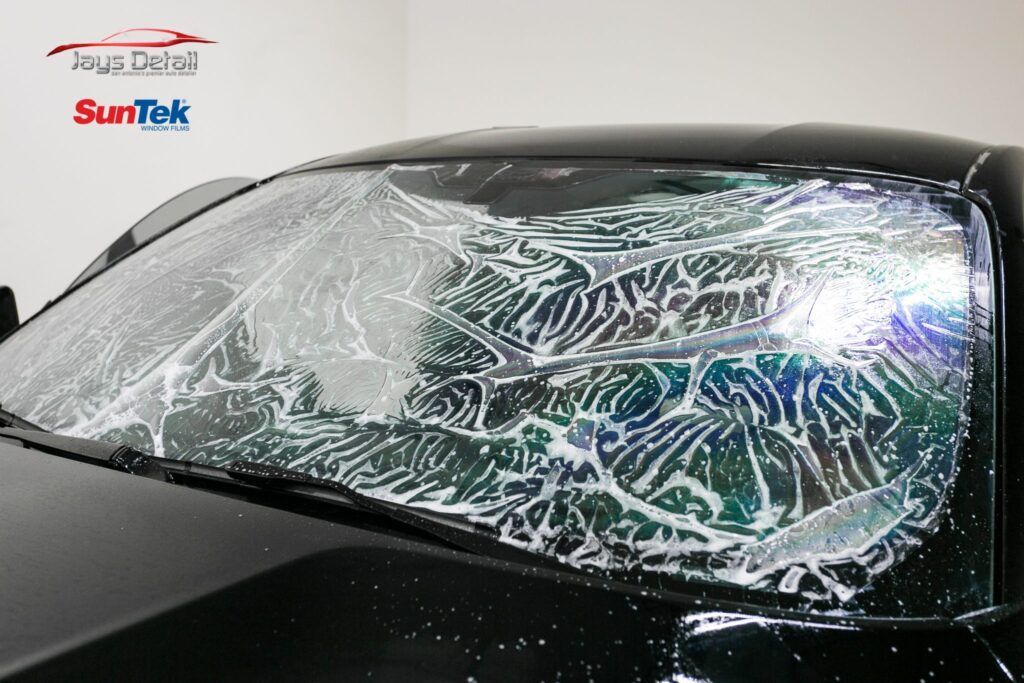 Windshield of a black car being treated with window tinting film; film is wet and translucent.