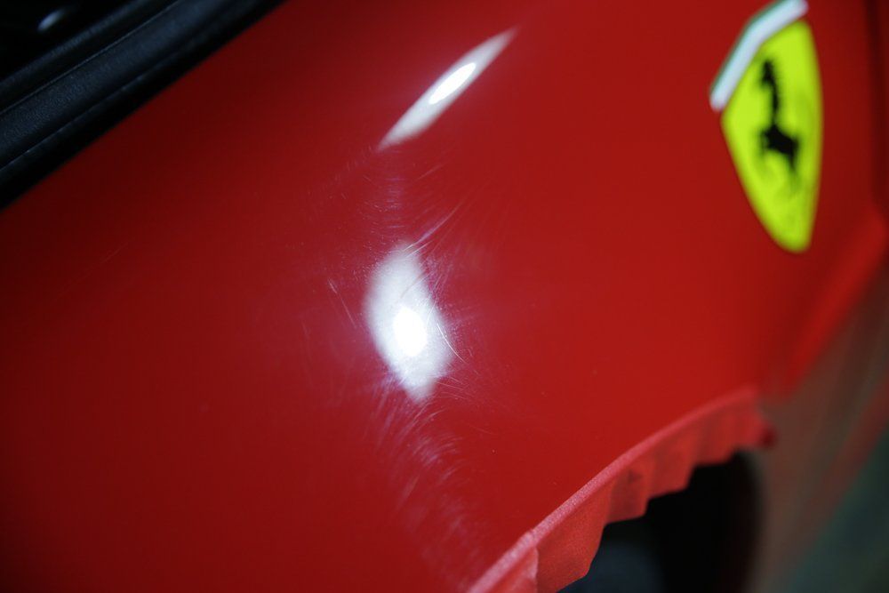 Red Ferrari car with visible scratches, near the emblem, partially covered with masking tape.