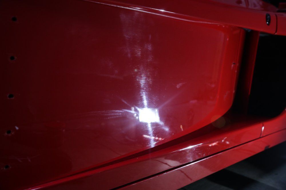Red car door with scratches, lit by a bright reflection.