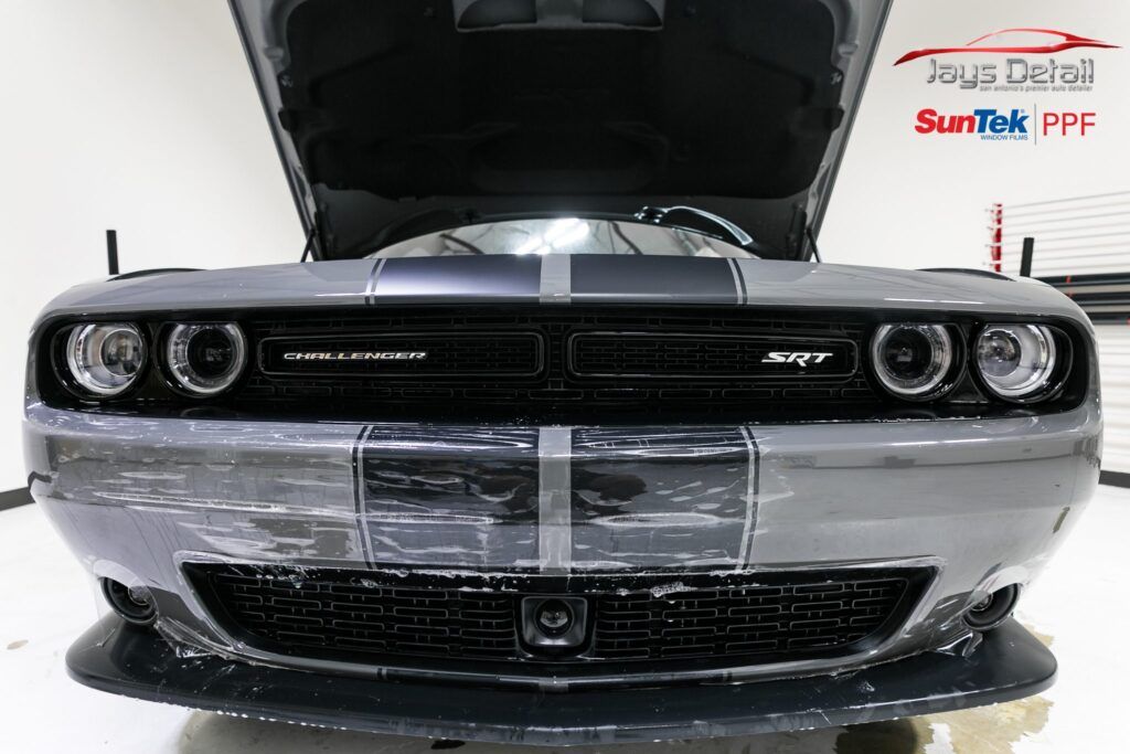 Front view of a gray Dodge Challenger with hood open, black stripes, and headlights on.