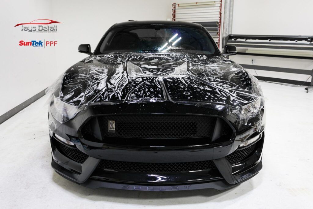 Black Mustang with a unique wrap on the hood, in a well-lit workshop.