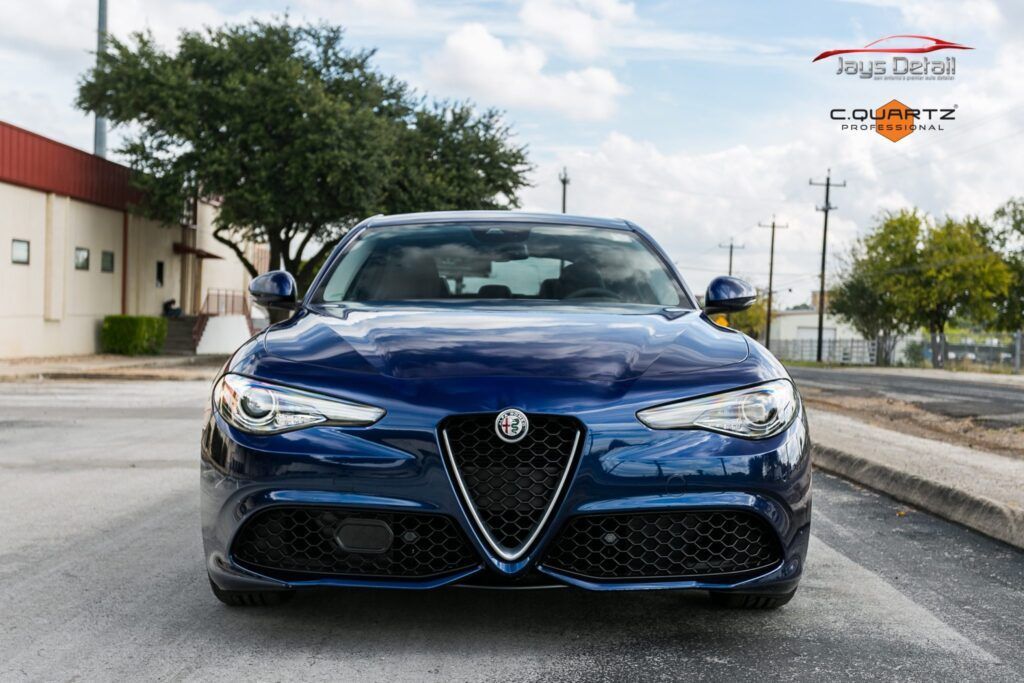 Blue Alfa Romeo Giulia sedan parked on a paved road, showcasing the front grille and headlights.