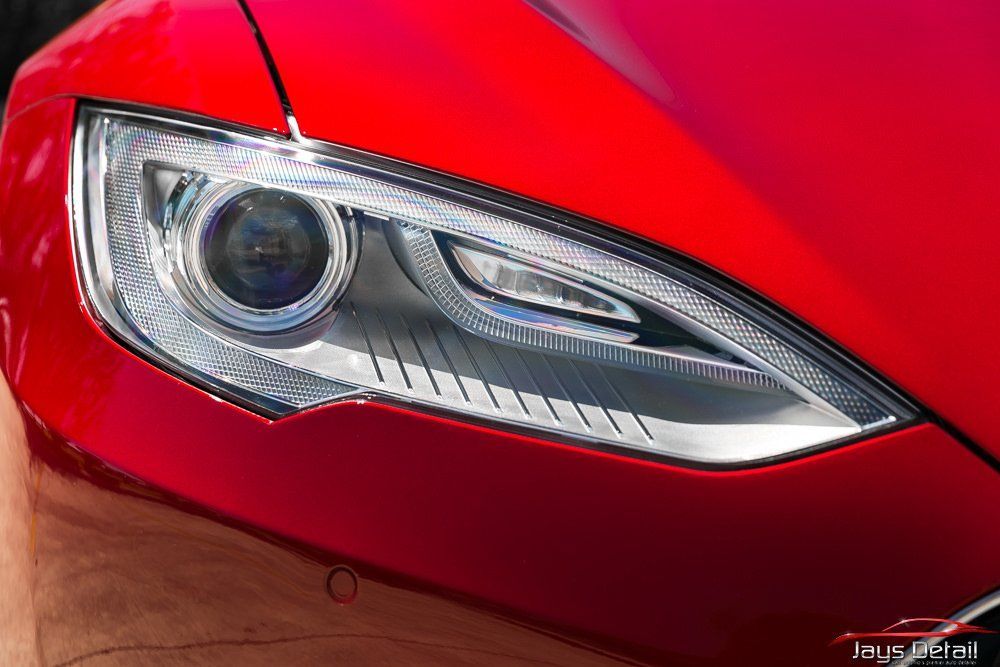 Red Tesla car headlight, close-up, showing detailed design and surrounding body.