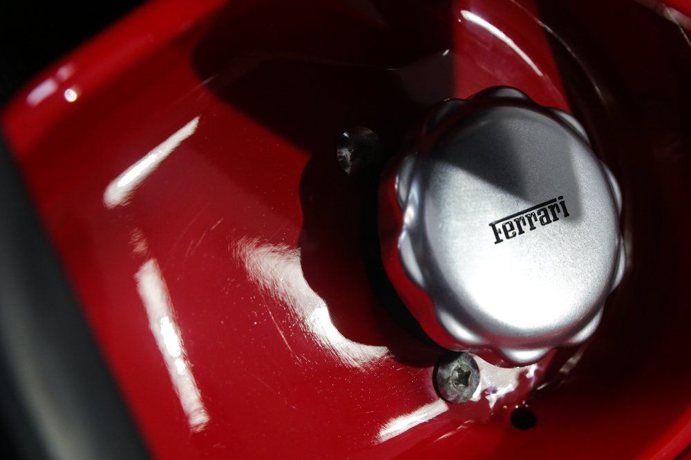Close-up of a red Ferrari fuel cap with the Ferrari logo, on a shiny red surface.