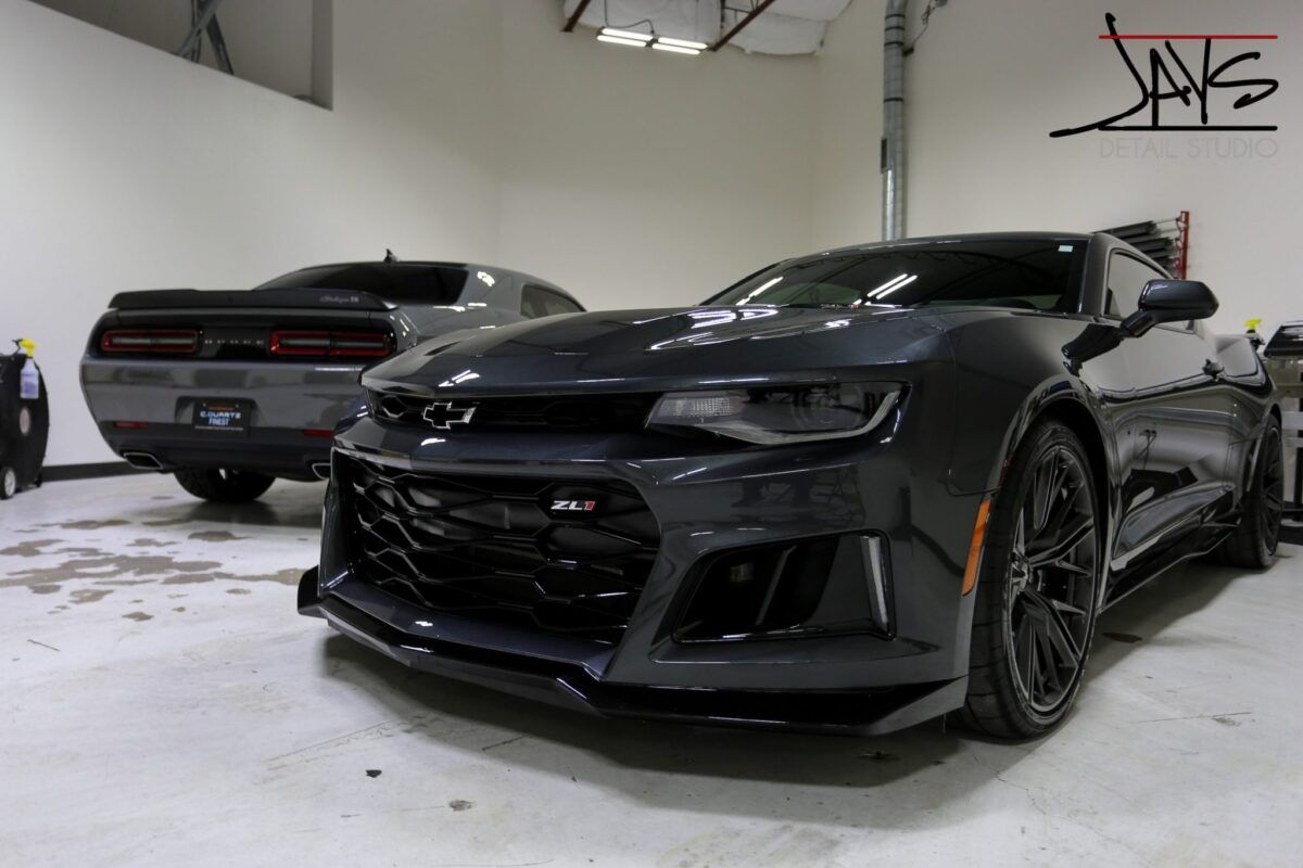 Gray Chevrolet Camaro and Dodge Challenger in a garage.